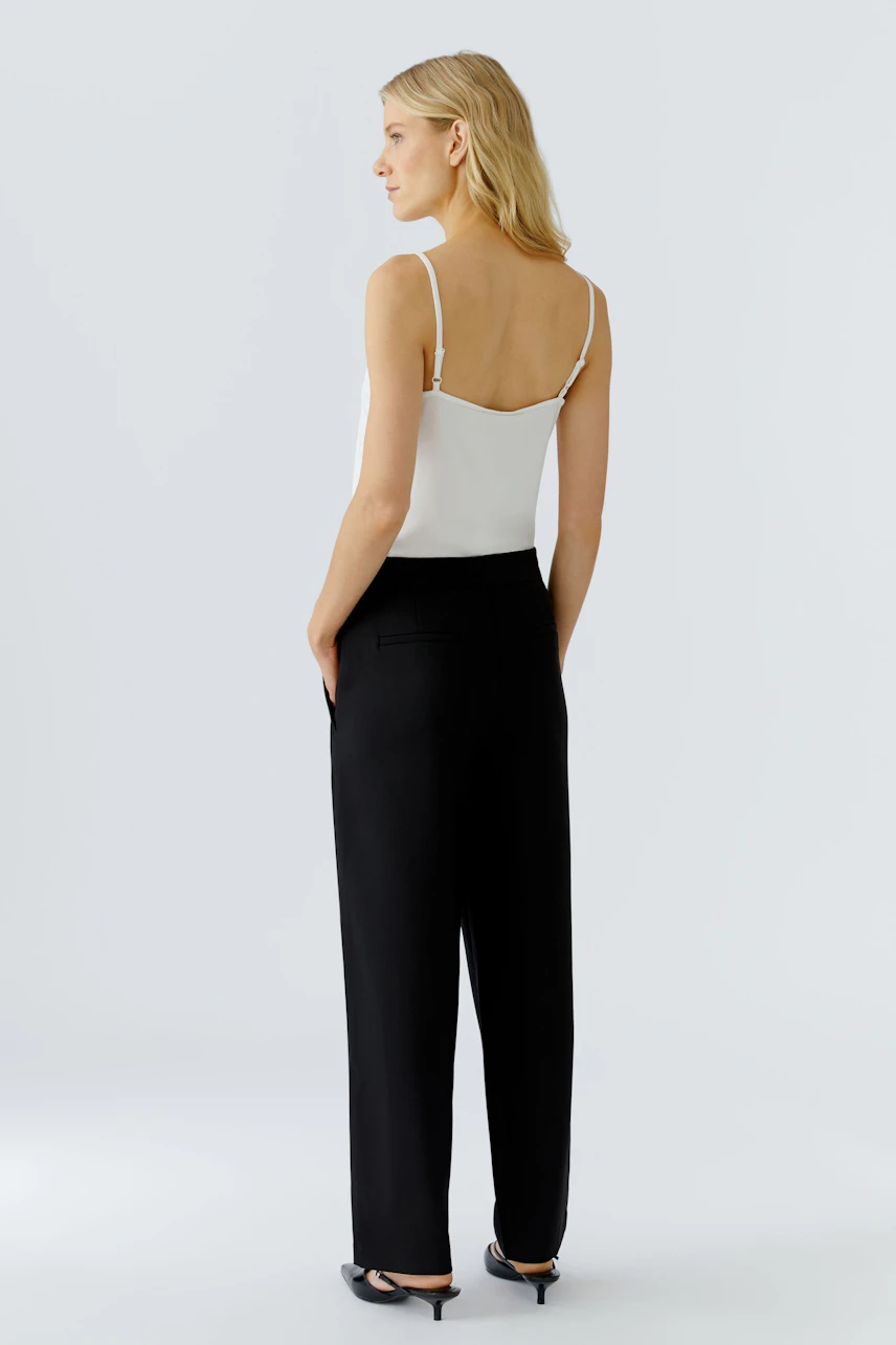 Stylish women's pleated trousers: A woman in black trousers and a white top, showcasing a modern look.