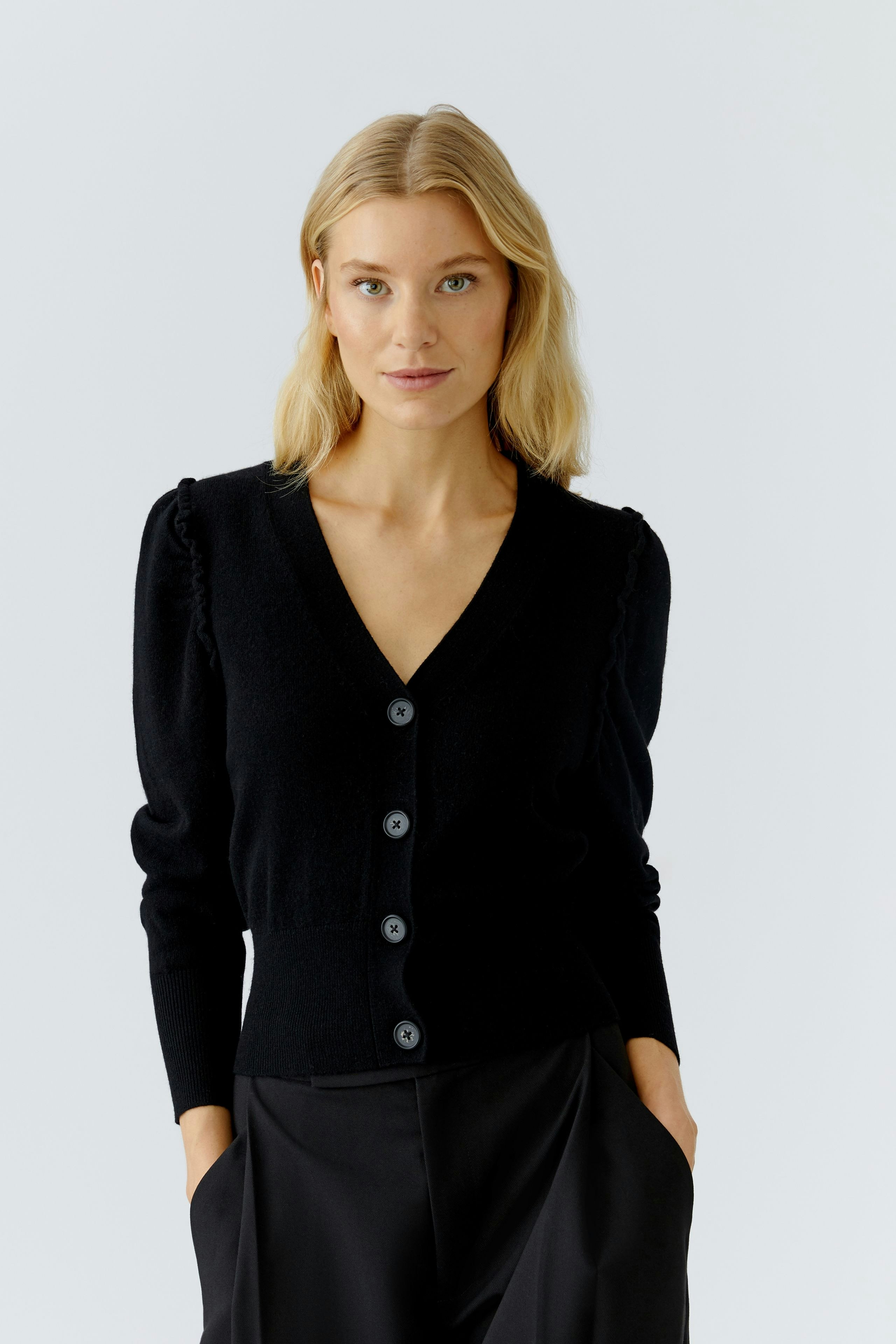 Modern women's cardigan: A woman in a black cardigan with buttons and puffed sleeves poses confidently.