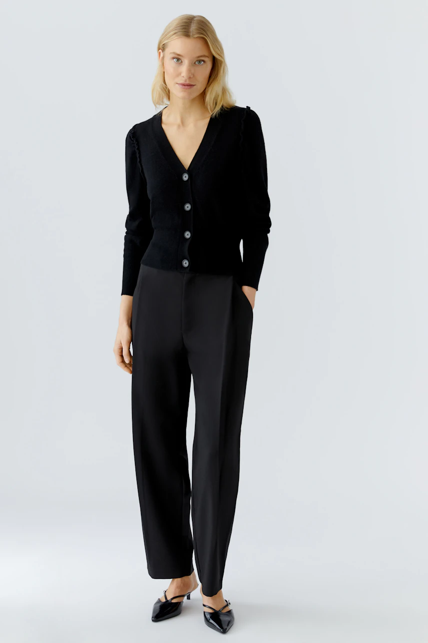 Casual women's cardigan: A woman in a black cardigan with buttons and relaxed-fit trousers.