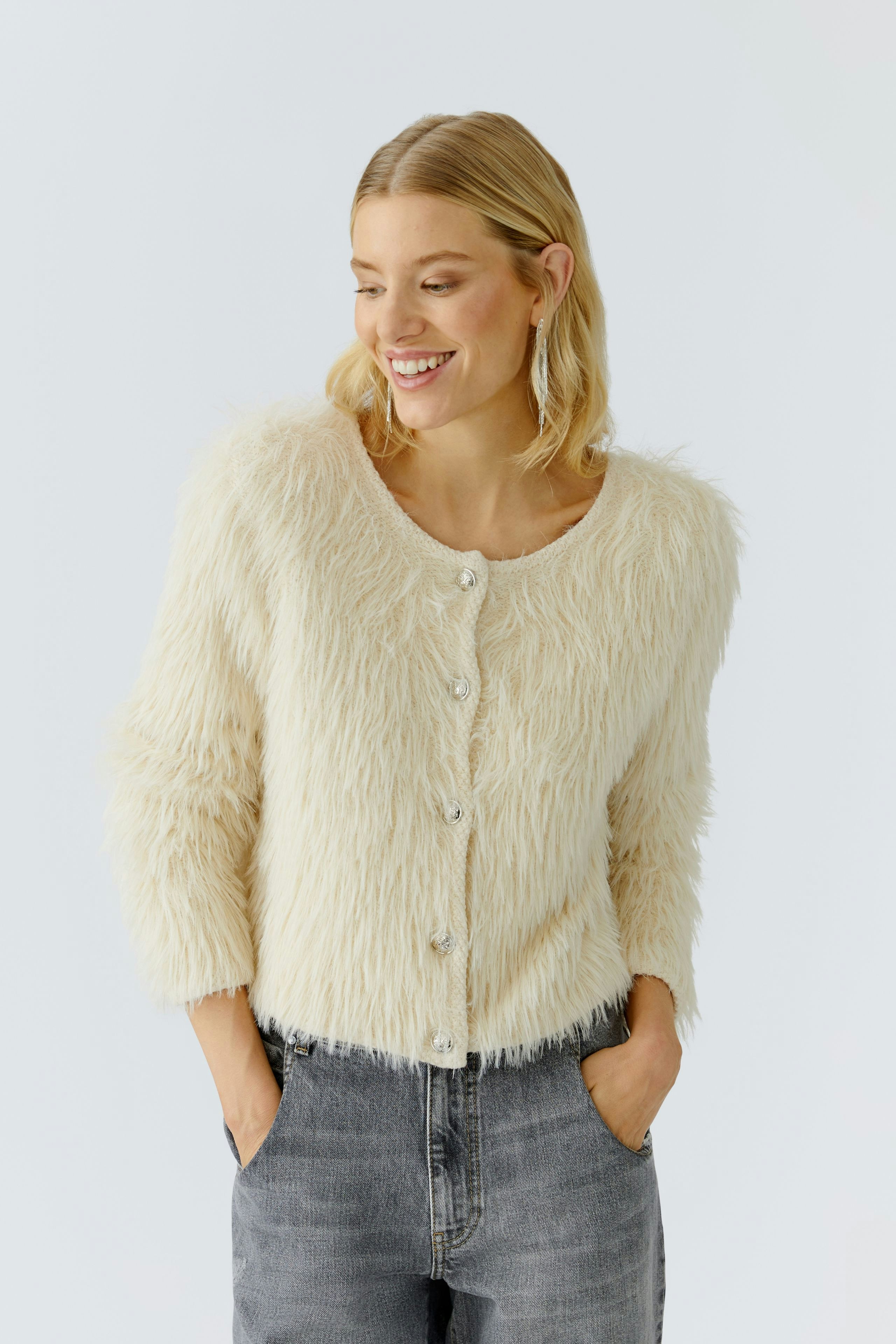 Cozy women's cardigan: Smiling woman in a fluffy cream cardigan with buttons and casual jeans.