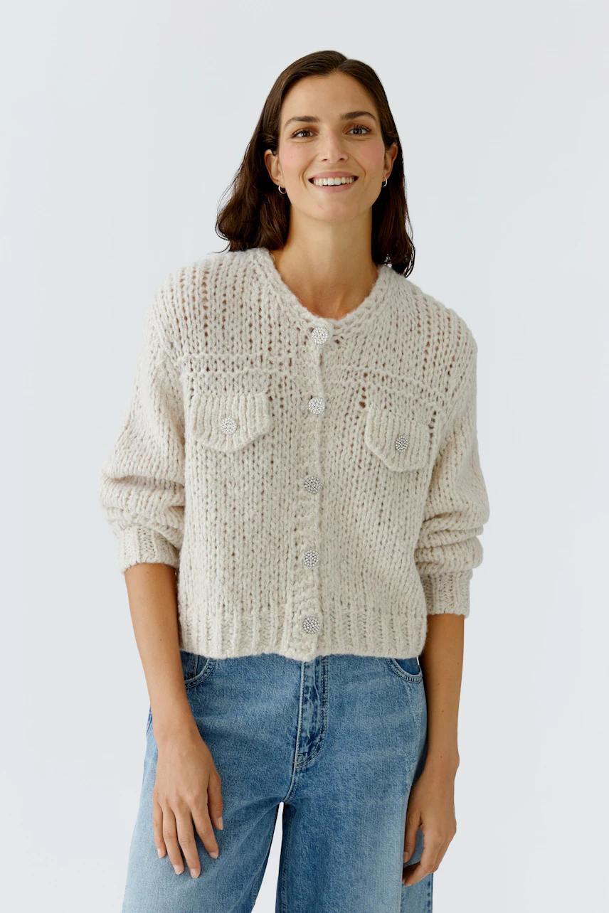 Casual women's cardigan: A woman in a light knitted cardigan with pockets and relaxed jeans smiles.