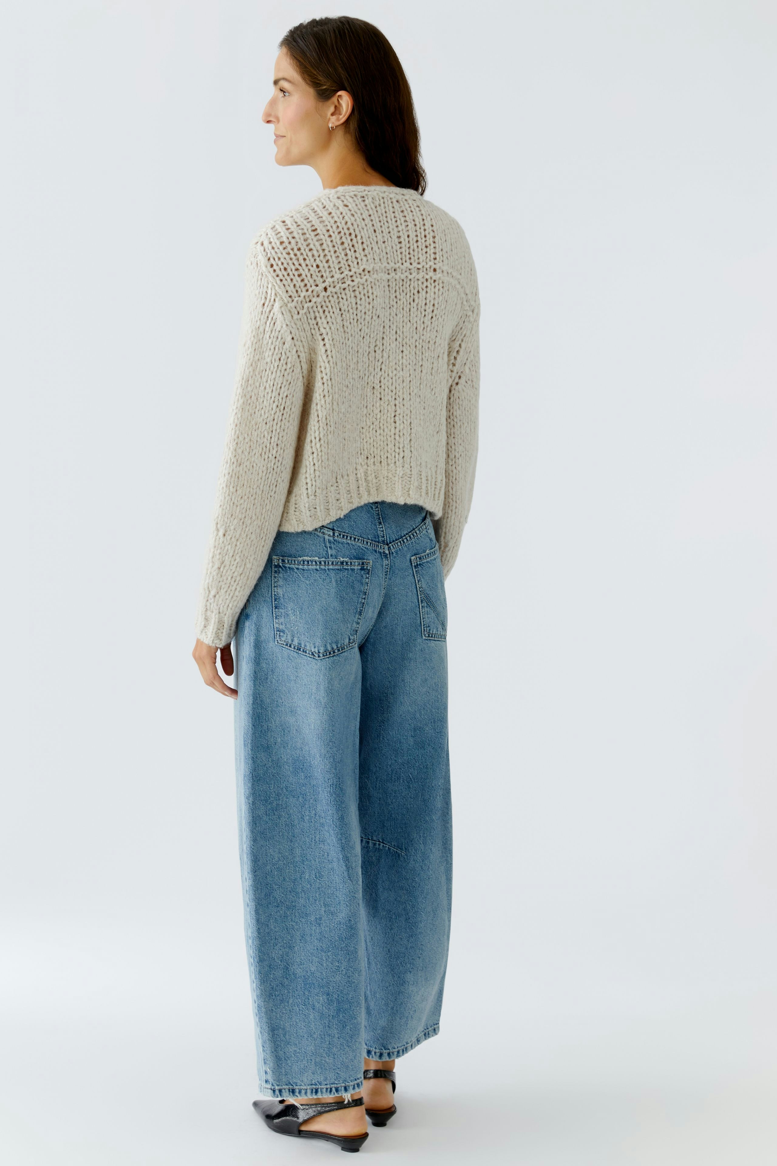 Bequeme Damen-Strickjacke: Frau mit lockerer, hellbeiger Strickjacke und weiten Jeans von hinten.