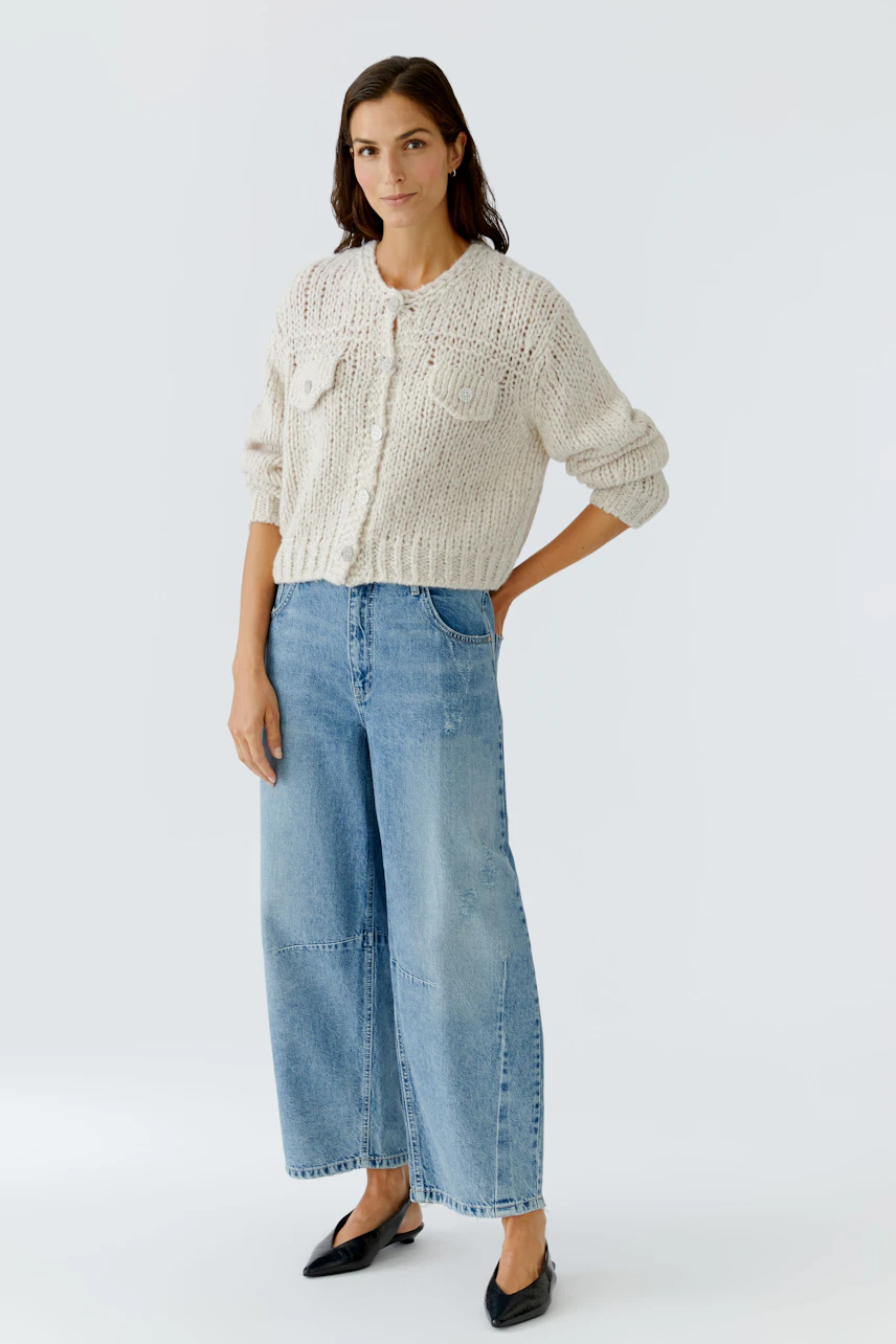 Casual women's cardigan: A woman in a chunky knit cardigan with pockets, paired with wide-leg jeans.