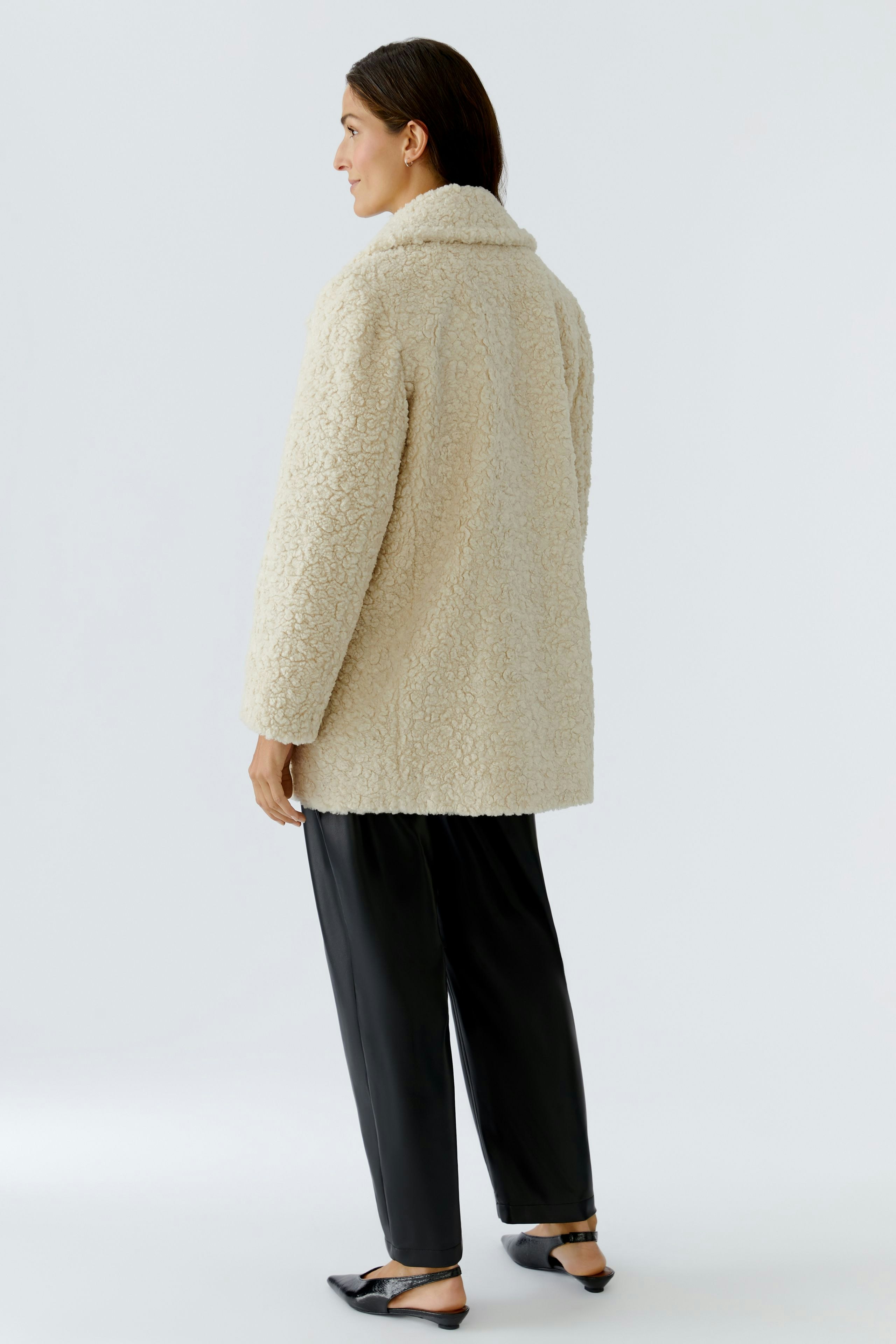 Cozy women's coat: A woman in a fluffy beige coat with a relaxed fit, paired with black pants.