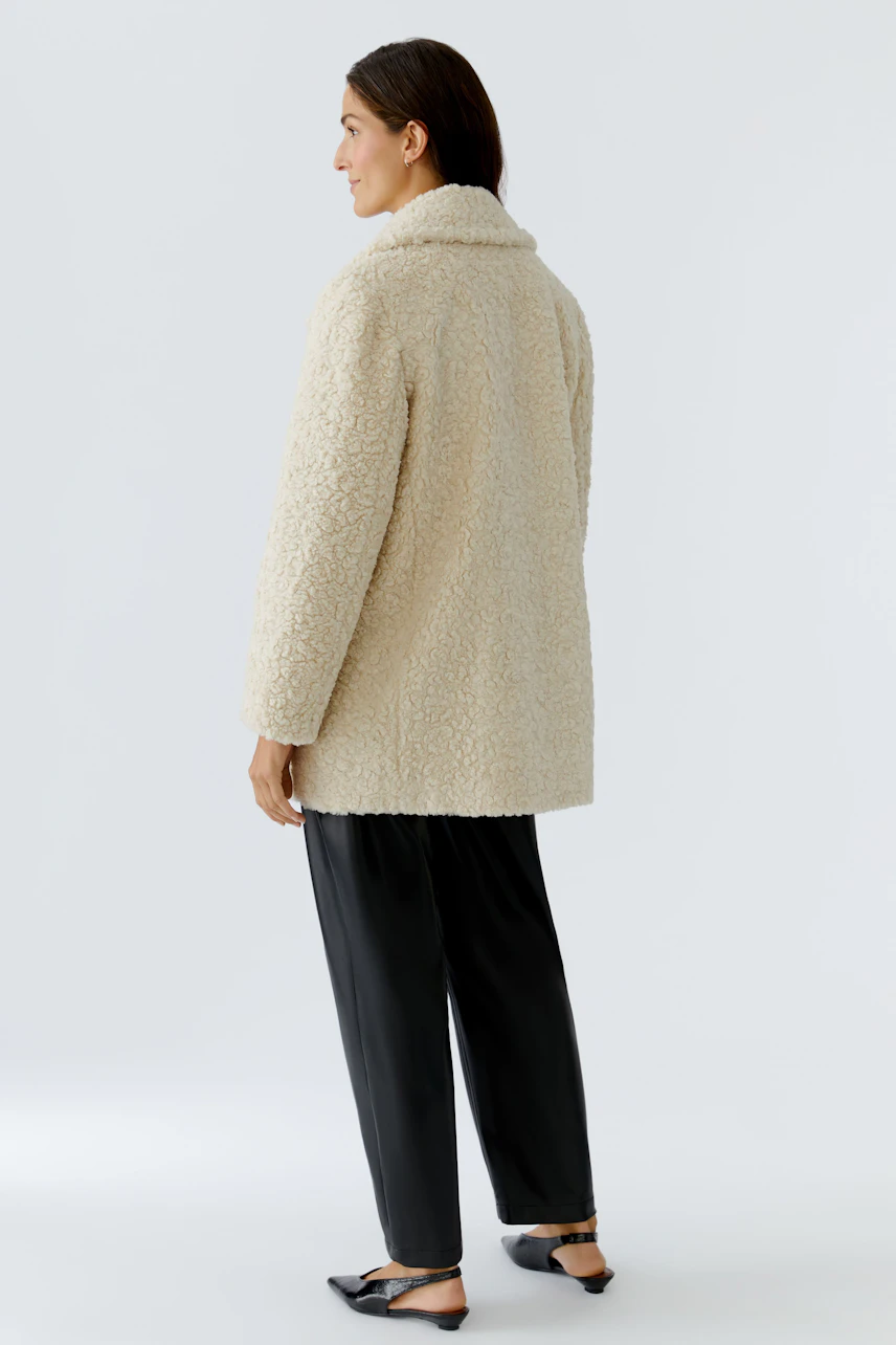 Cozy women's coat: A woman in a fluffy beige coat with a relaxed fit, paired with black pants.