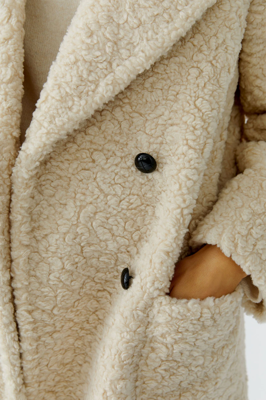 Cozy women's coat: A woman in a soft, textured cream coat with black buttons and pockets.