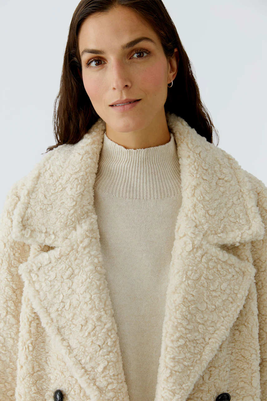 Cozy women's coat: A woman in a fluffy cream coat with a soft collar and buttons.