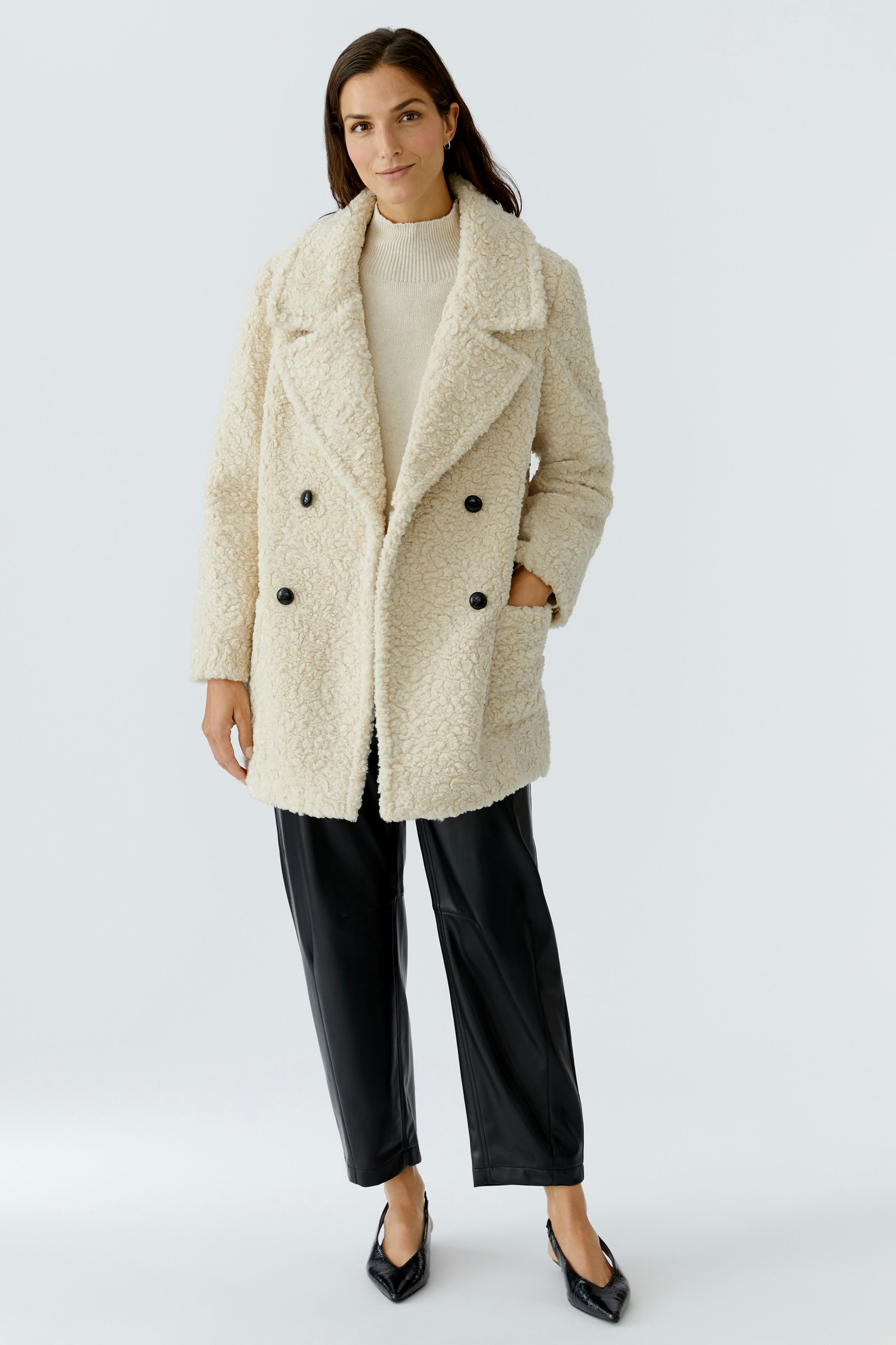 Cozy women's coat: A woman in a fluffy cream coat with double-breasted buttons and side pockets.