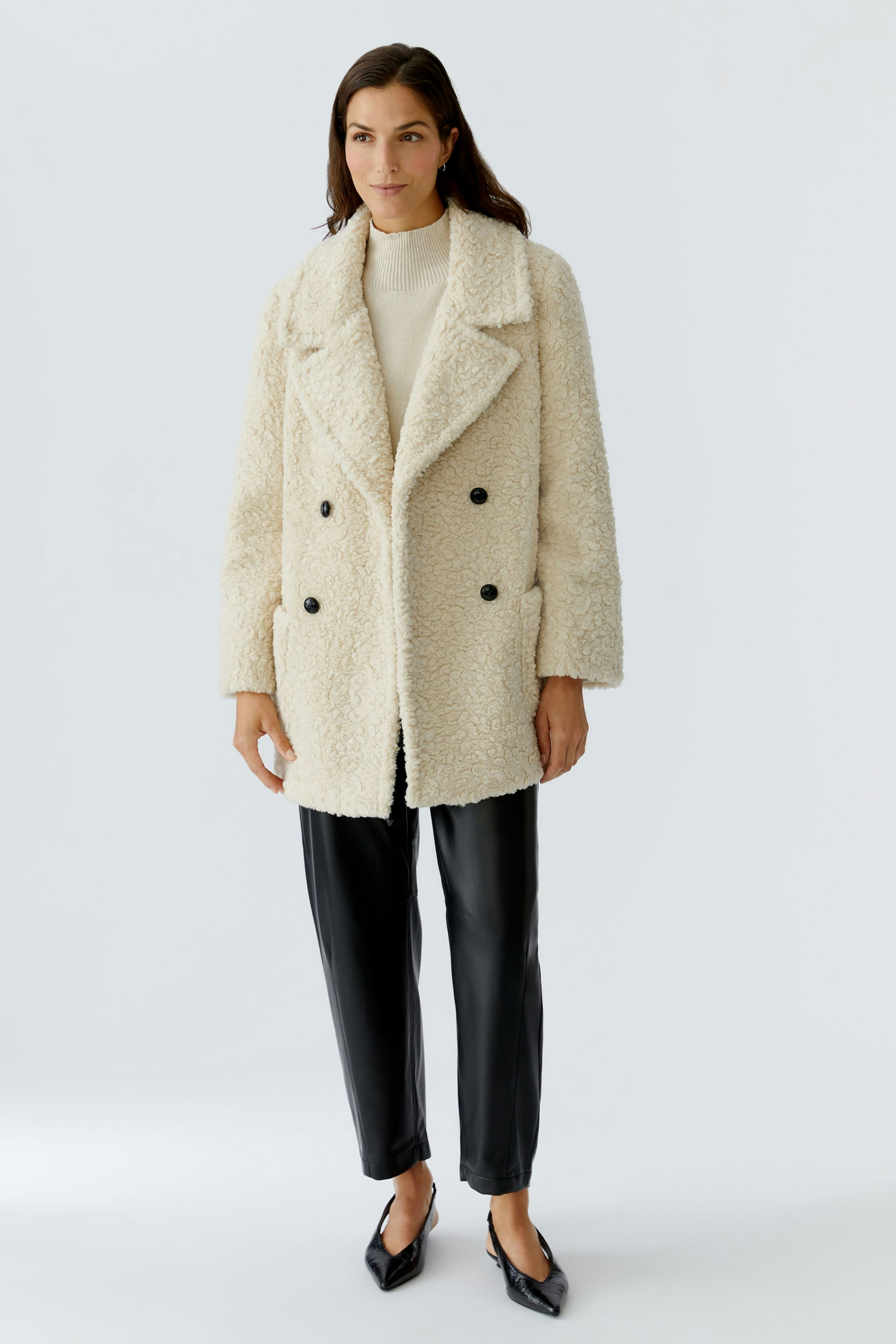 Cozy women's coat: A woman in a fluffy cream double-breasted coat with black buttons and relaxed fit pants.