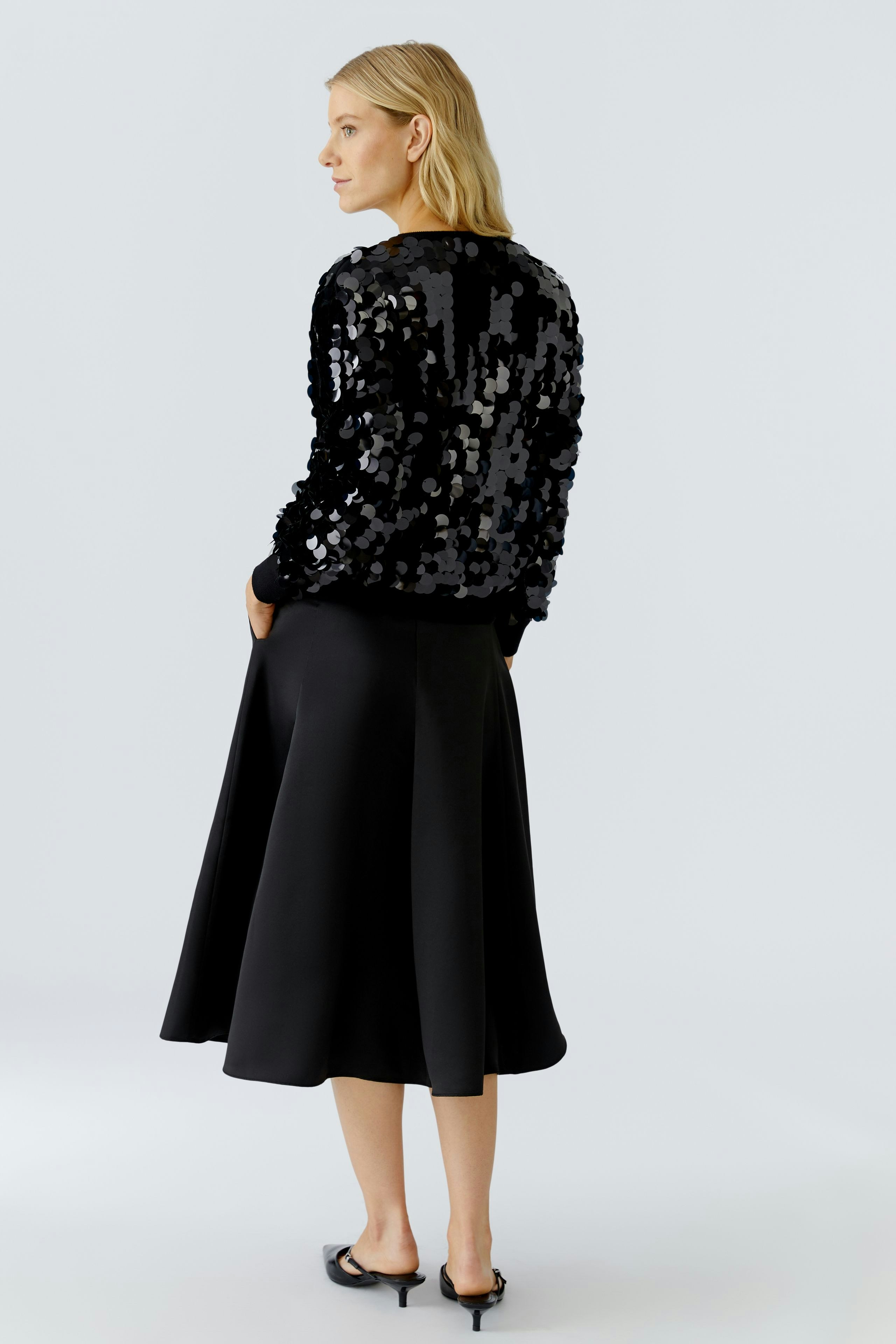 Modern women's pullover: Woman in a black sequined pullover paired with a flowing black skirt.