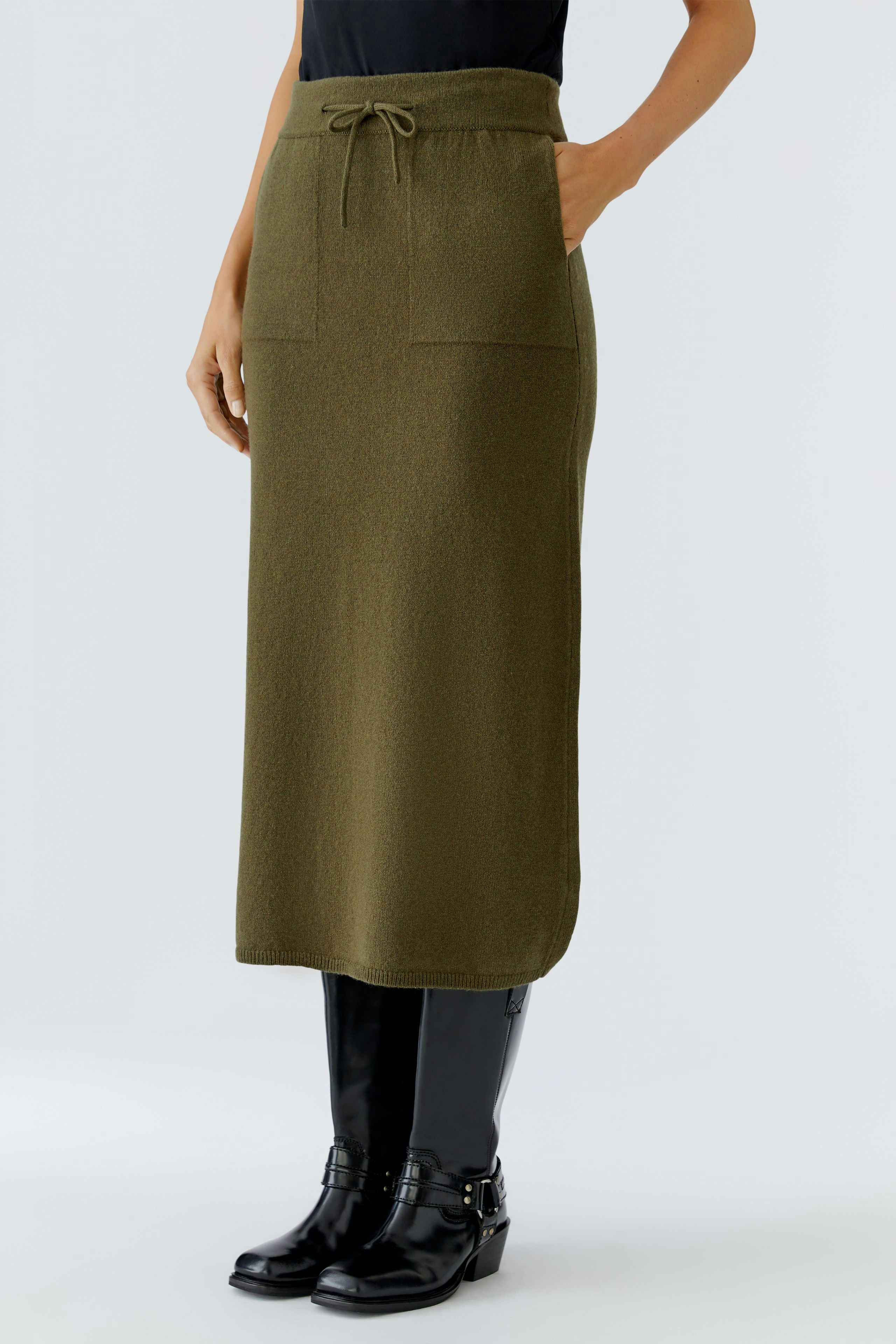 Casual women's knitted skirt in olive green with pockets and drawstring, paired with stylish black boots.