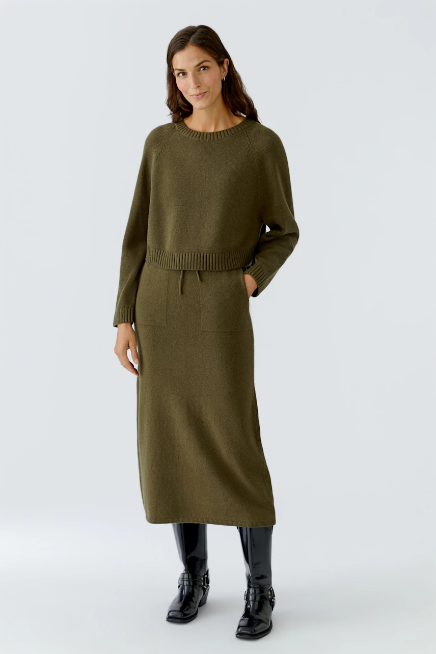 Casual women's knitted skirt: A woman in an olive green knitted skirt with a relaxed fit and pockets.