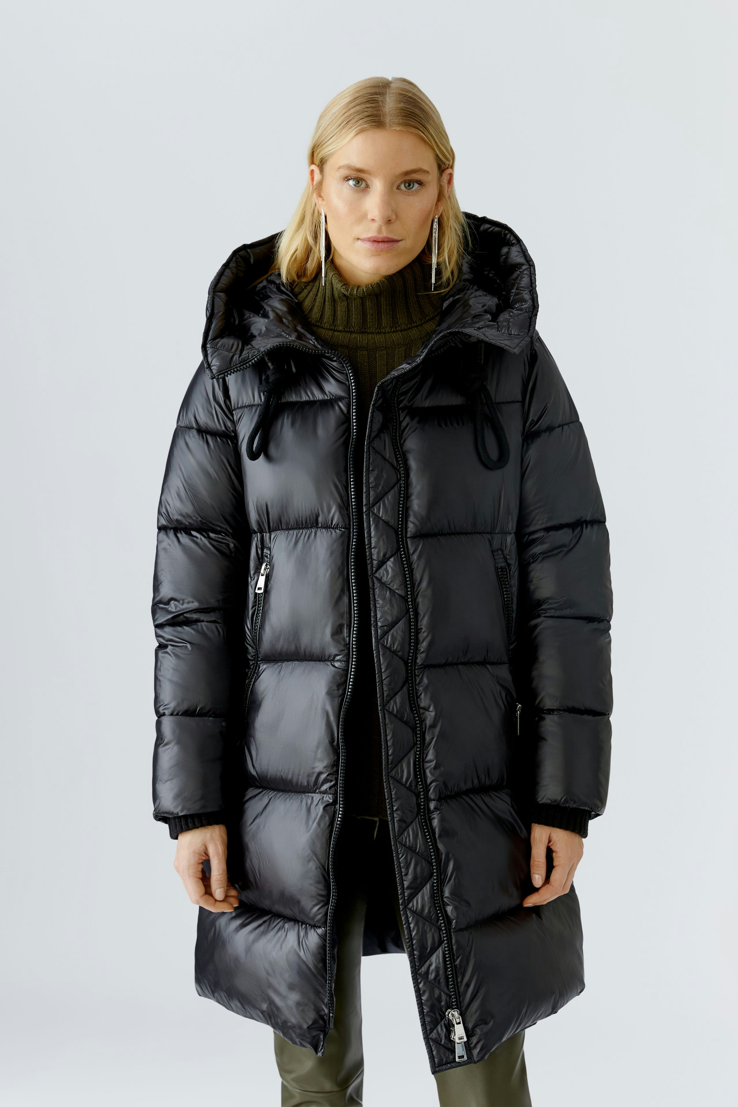 Modern women's winter coat: Woman in a black puffer coat with a hood, styled with a green sweater.