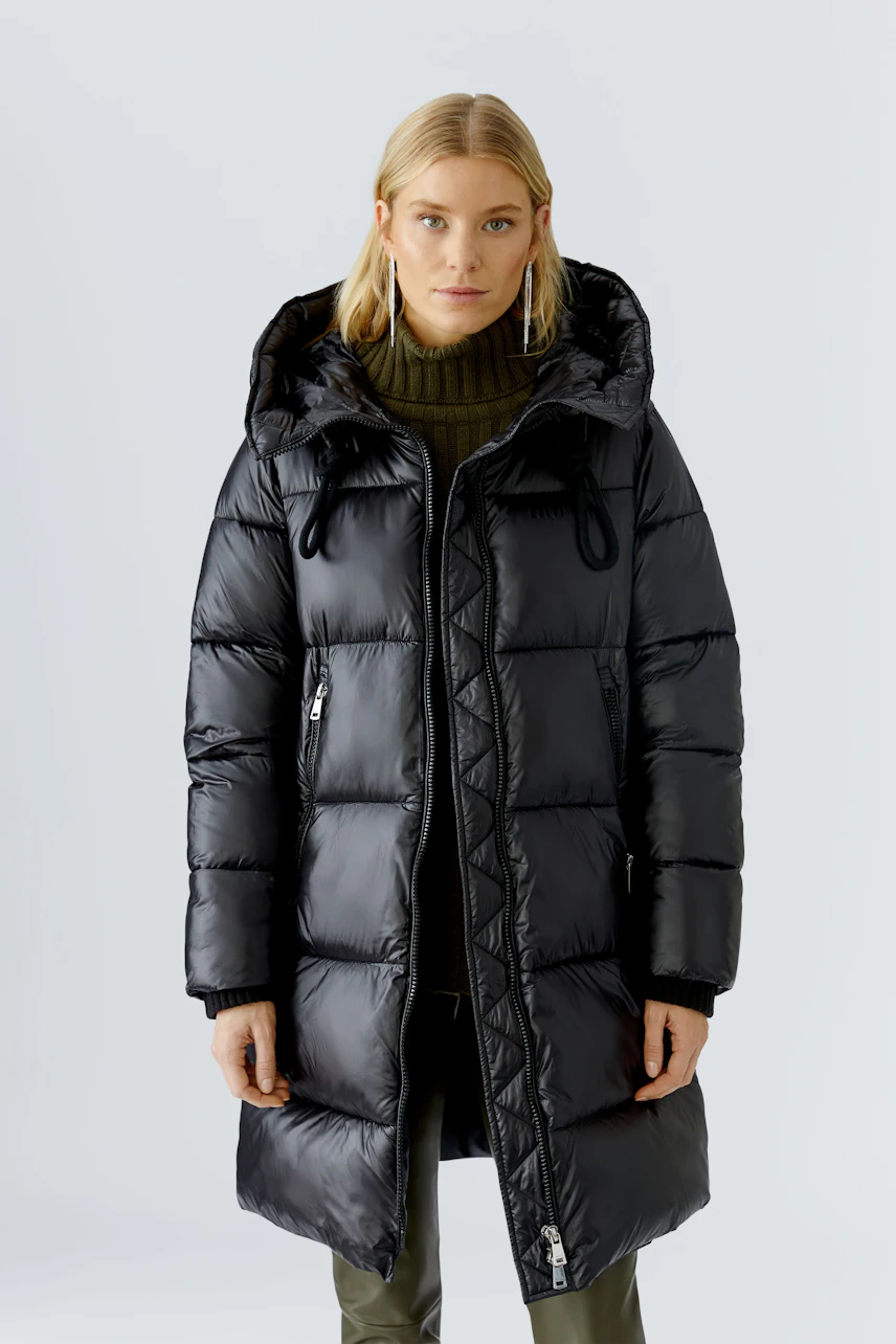 Modern women's winter coat: Woman in a black puffer coat with a hood, styled with a green sweater.