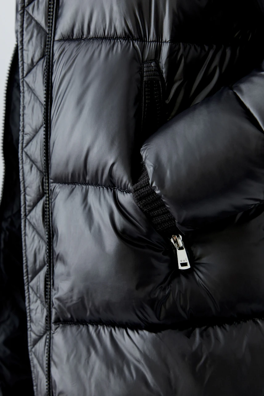 Warm women's winter coat in shiny black with a zippered pocket and quilted design.