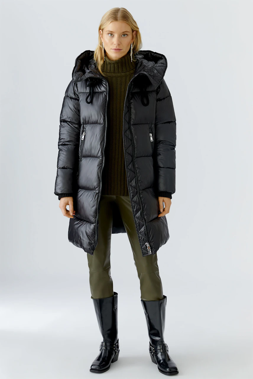 Stylish women's winter coat: A woman in a black puffer coat with a hood, paired with green pants.