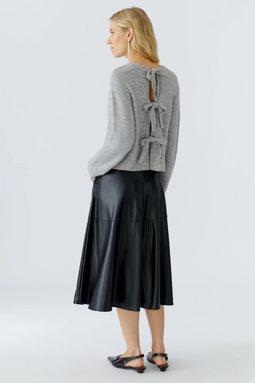 Damen-Pullover in Grau mit verspieltem Rückendetail und lässigem Schnitt, kombiniert mit einem schwarzen Rock.