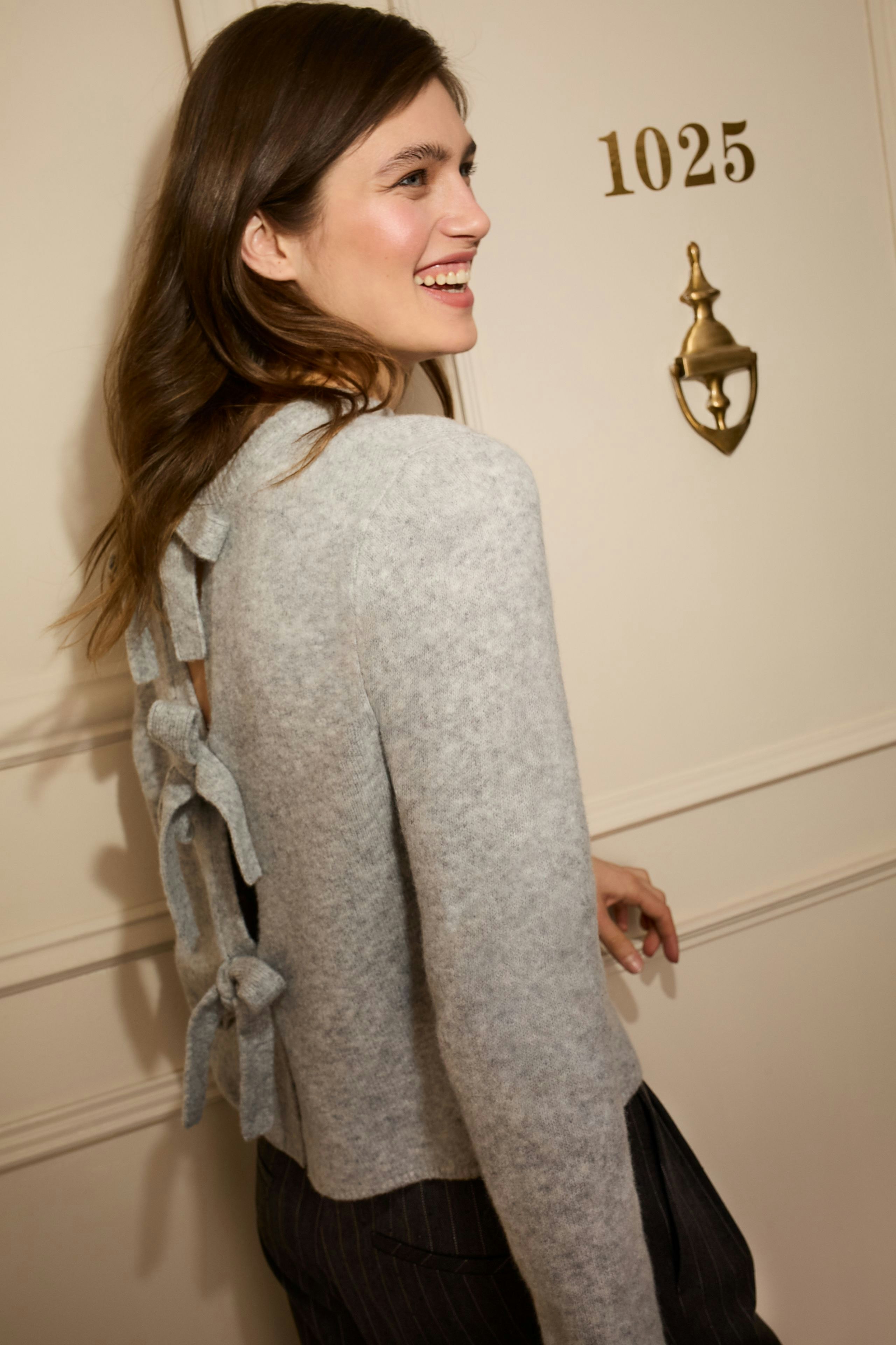 Casual women's pullover: Smiling woman in a grey pullover with bow details at the back.
