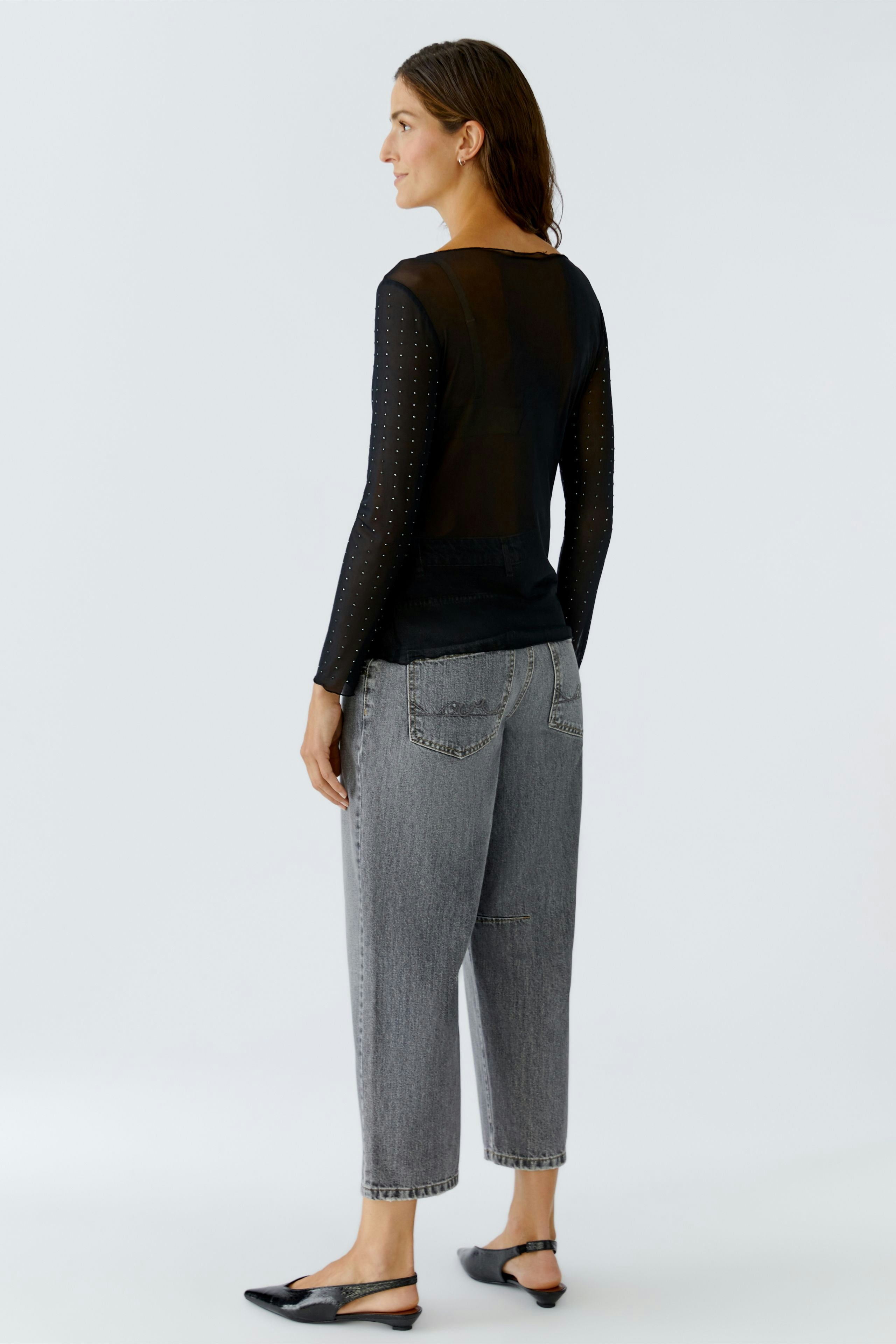 Damen Langarmshirt: Frau in schwarzem Shirt mit transparenten Ärmeln und lässigen Jeans.