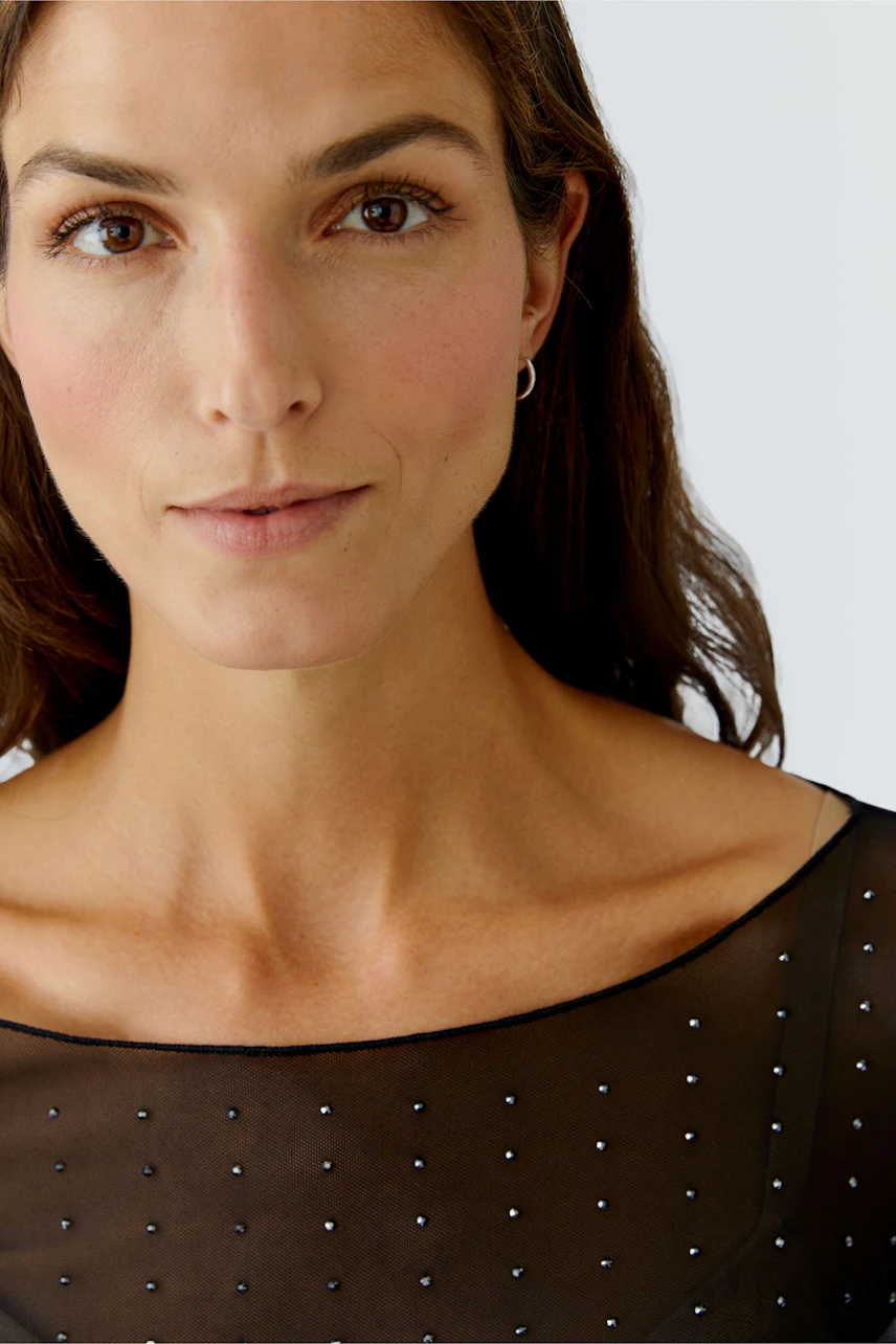 Stylish women's long-sleeve shirt: A woman in a sheer black top with subtle embellishments.