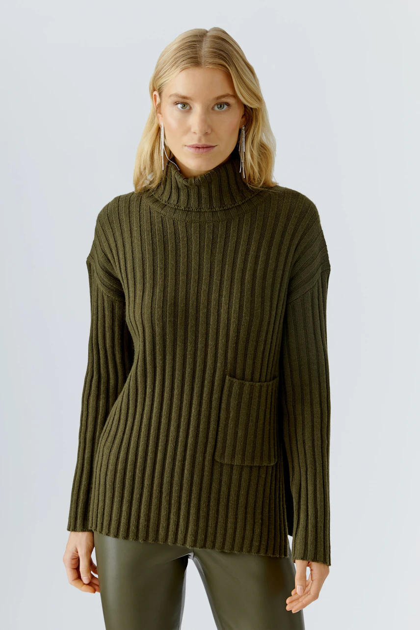 Modern women's pullover: A woman in a ribbed olive green pullover with a high collar and pocket.