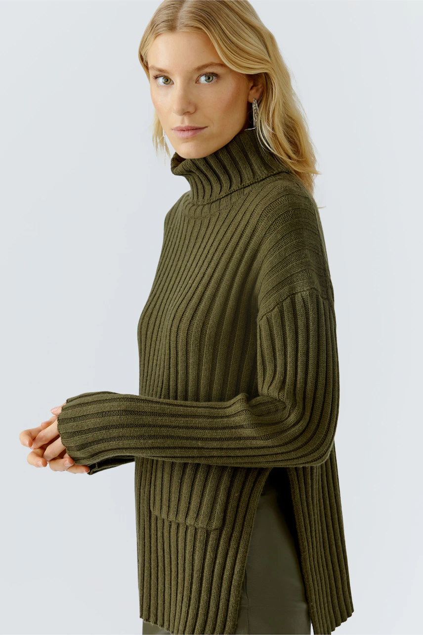 Casual women's pullover: A woman in a ribbed olive green pullover with a high collar and side slits.