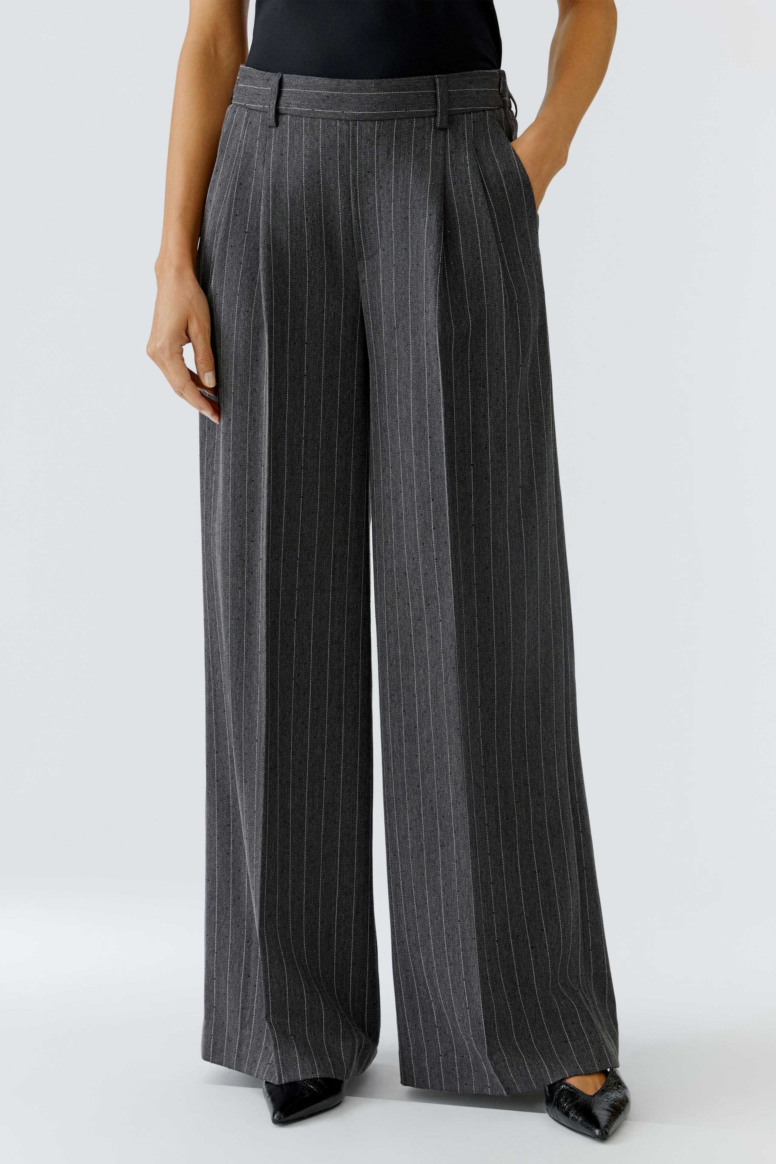 Wide-leg trousers: Woman in pinstriped, high-waisted trousers with a relaxed fit and side pockets.