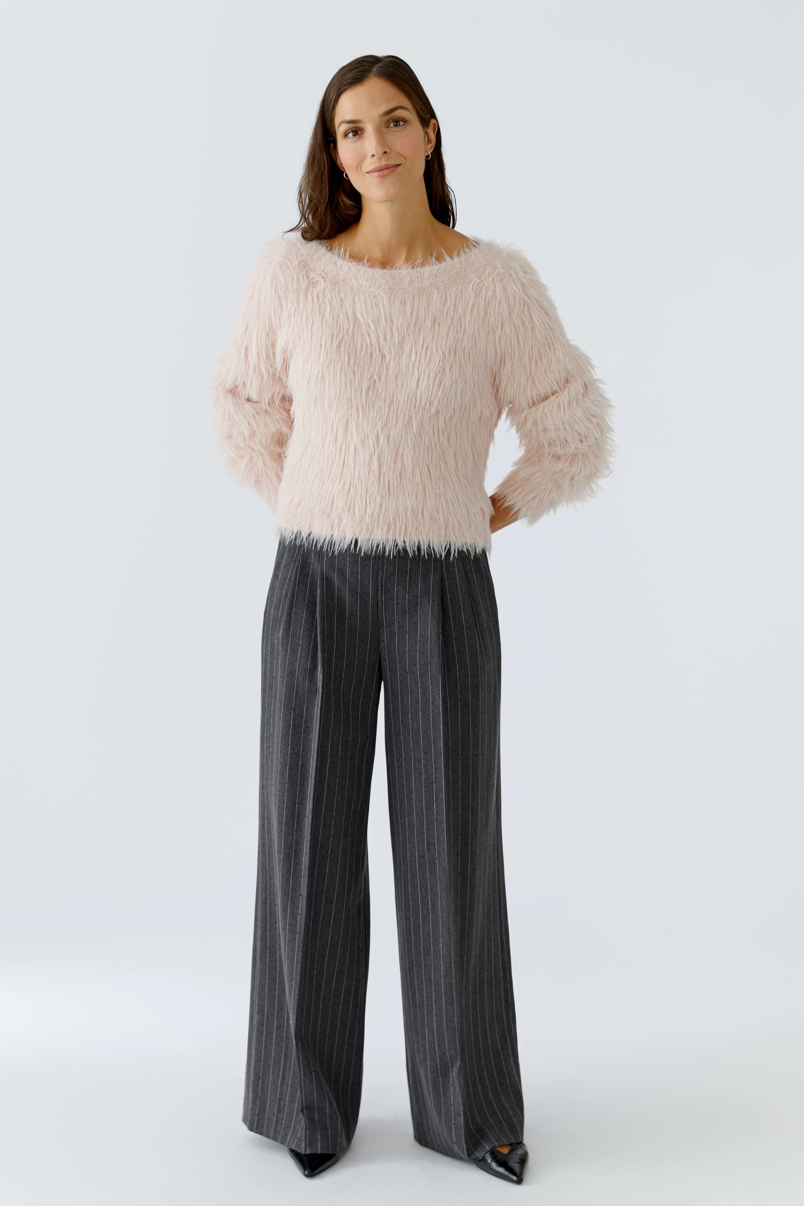 Damen-Bundfaltenhose: Frau in grauer, gestreifter Bundfaltenhose und flauschigem, rosa Pullover.