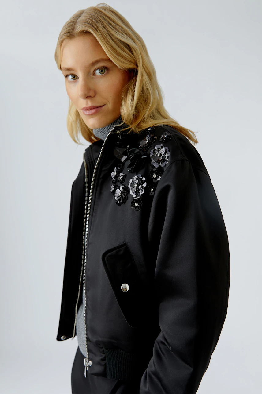 Stylish women's blouson: Young woman in a black bomber jacket with floral embellishments.