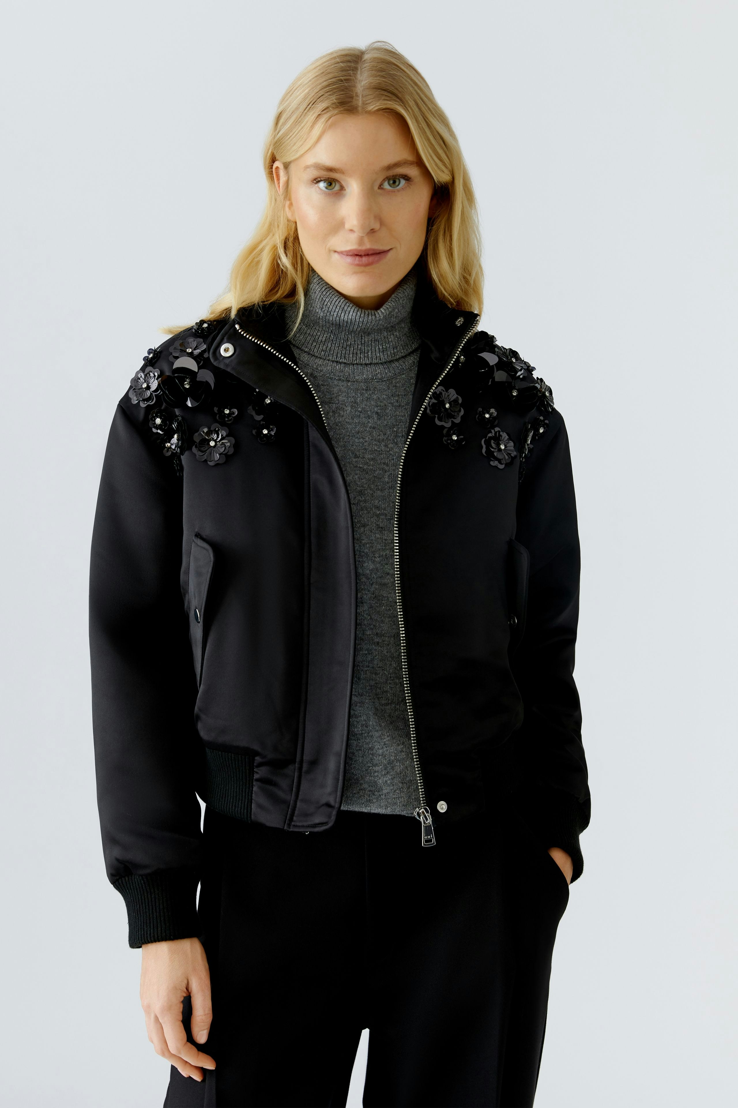 Modern women's blouson: Woman in a black bomber jacket with floral embellishments, paired with a turtleneck.