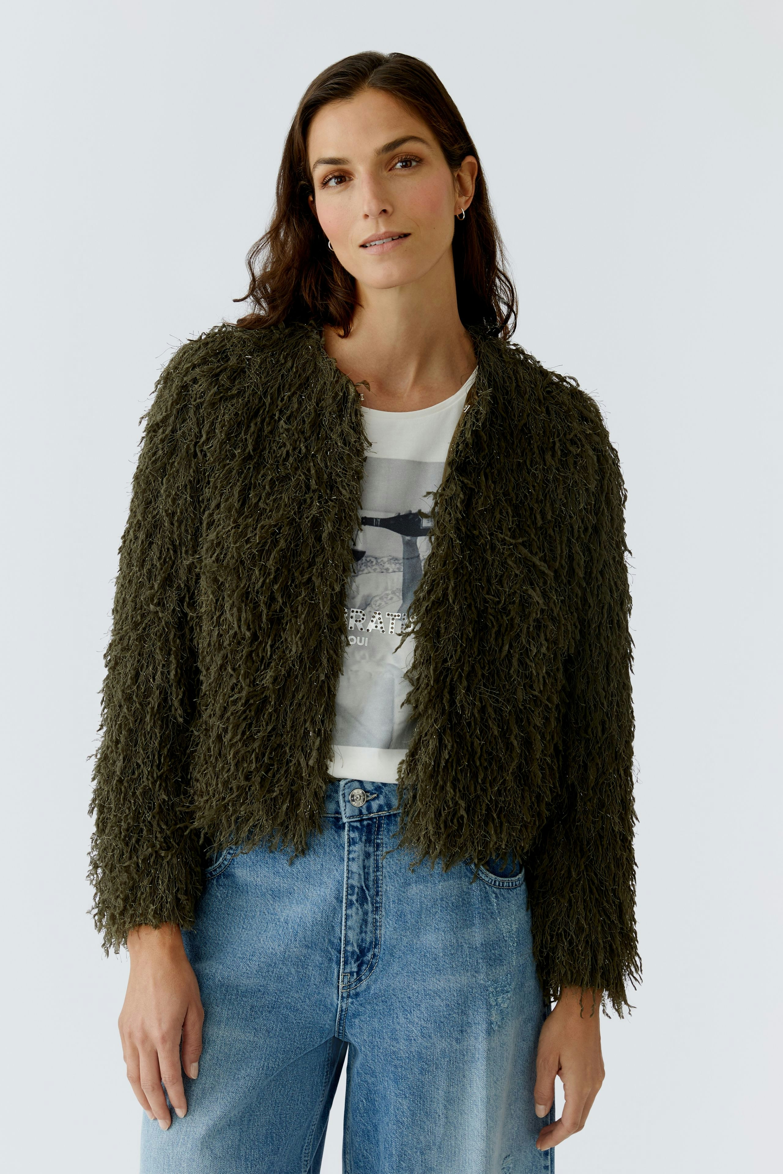 Casual women's jacket: A woman in a fluffy olive green jacket over a graphic tee and relaxed jeans.