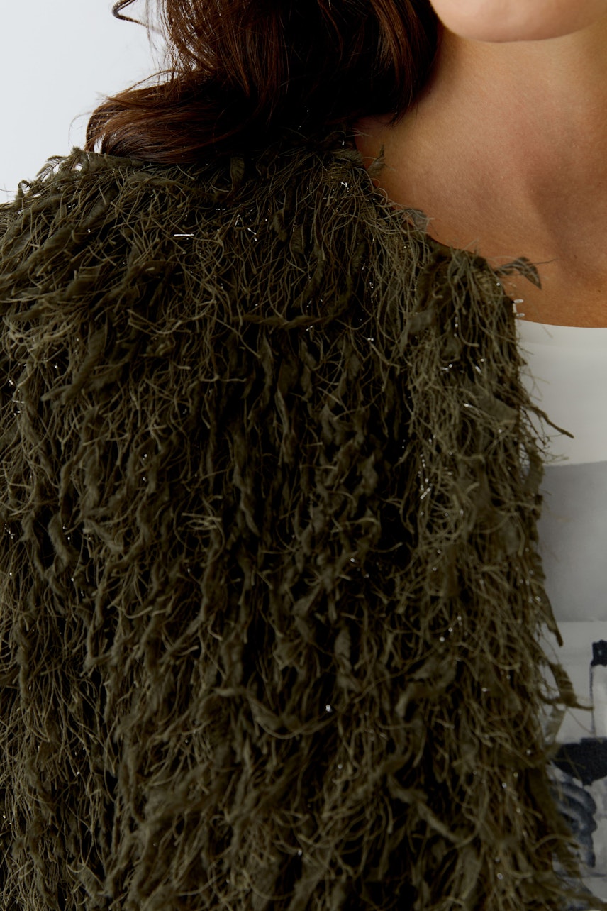 Moderne Damen-Jacke: Frau trägt eine grüne, strukturierte Jacke mit fransigen Details.