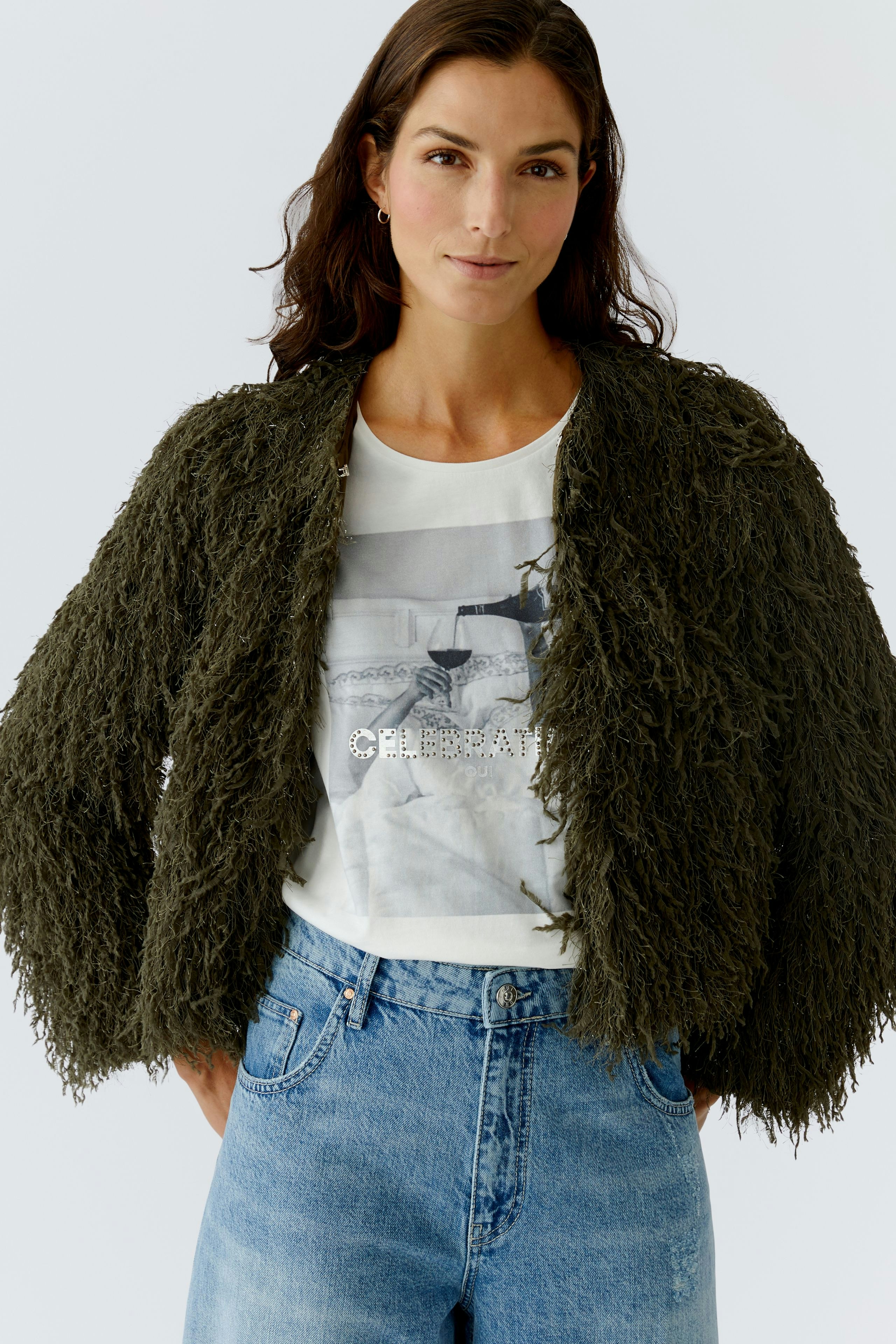 Casual women's jacket: A woman in a fluffy olive green jacket over a graphic tee and jeans.