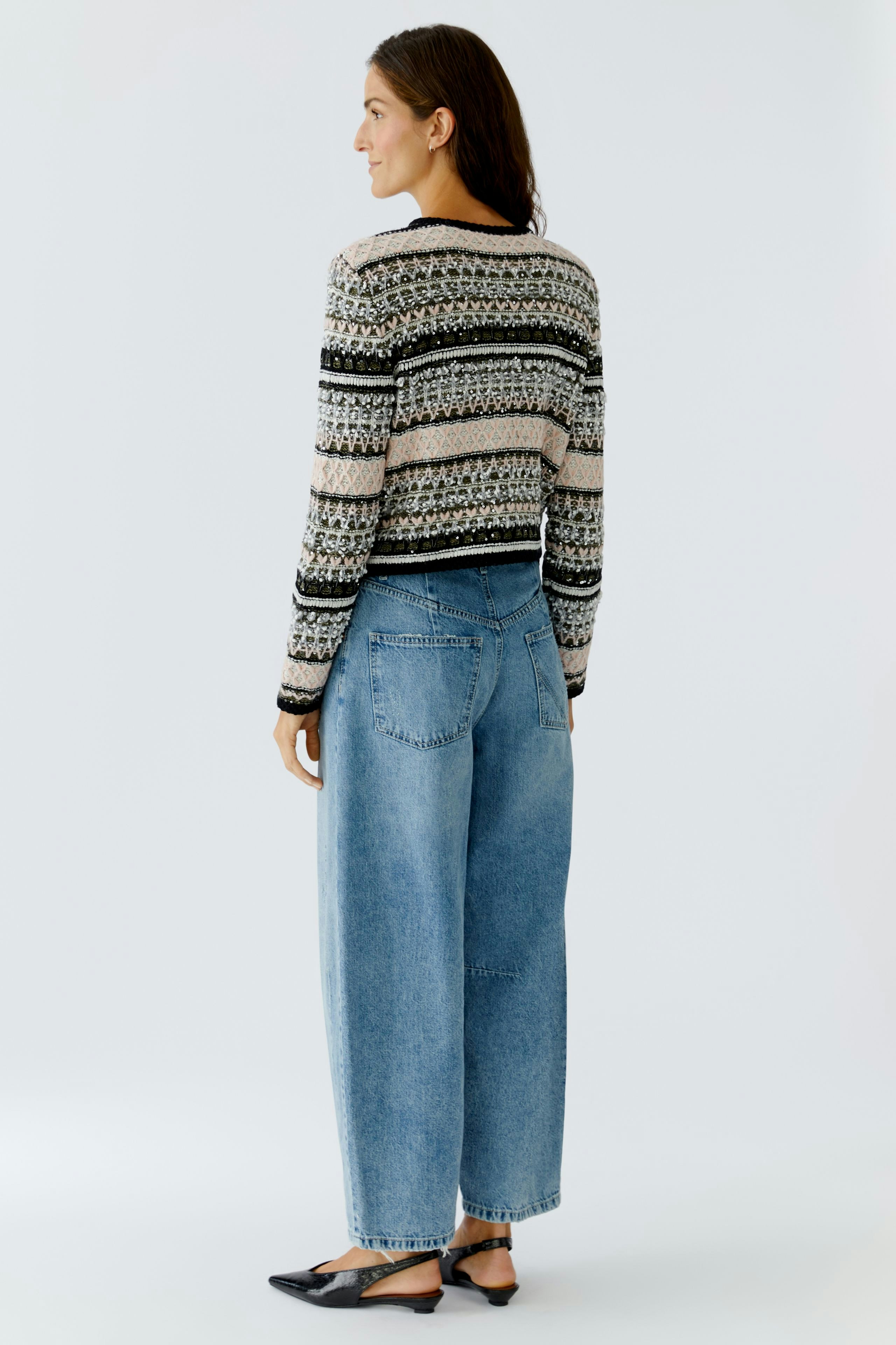 Casual women's cardigan: A woman in a patterned pullover, paired with wide jeans, stands confidently.