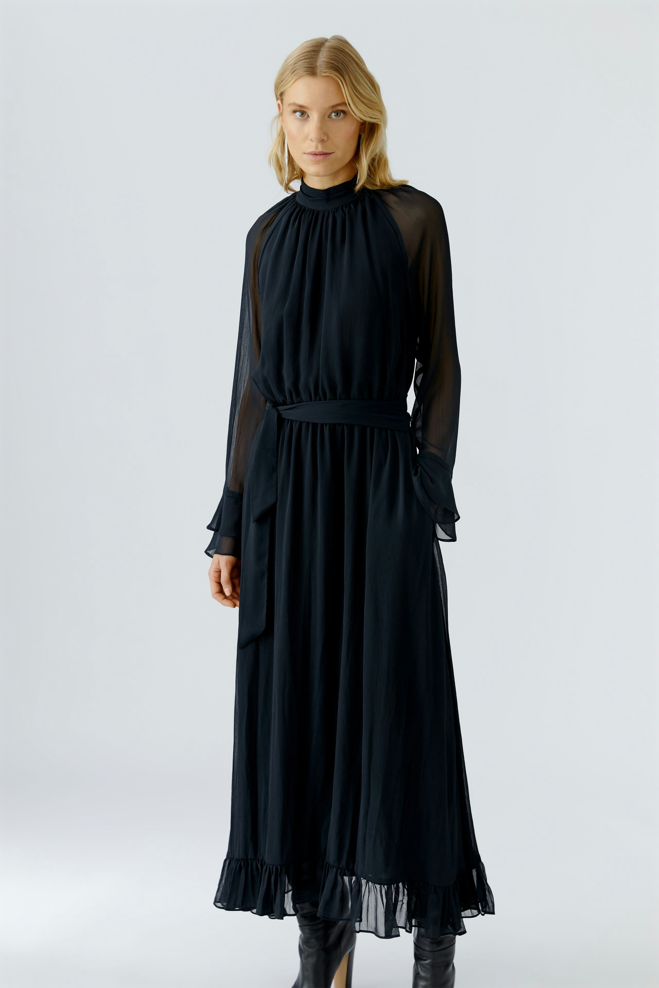 Flowy maxi dress: Woman in a black dress with sheer sleeves and a ruffled hem, exuding a relaxed vibe.