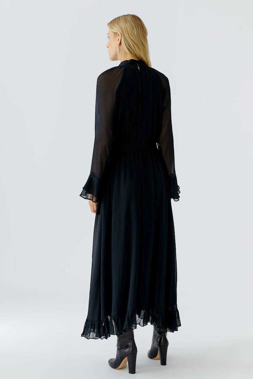 Maxikleid: Frau in schwarzem, fließendem Maxikleid mit Rüschendetails und langen Ärmeln.