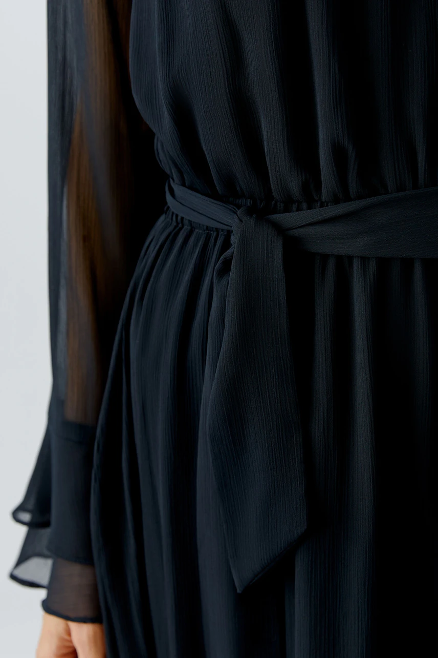 Maxikleid: Frau in schwarzem, fließendem Kleid mit Taillengürtel und transparenten Ärmeln.
