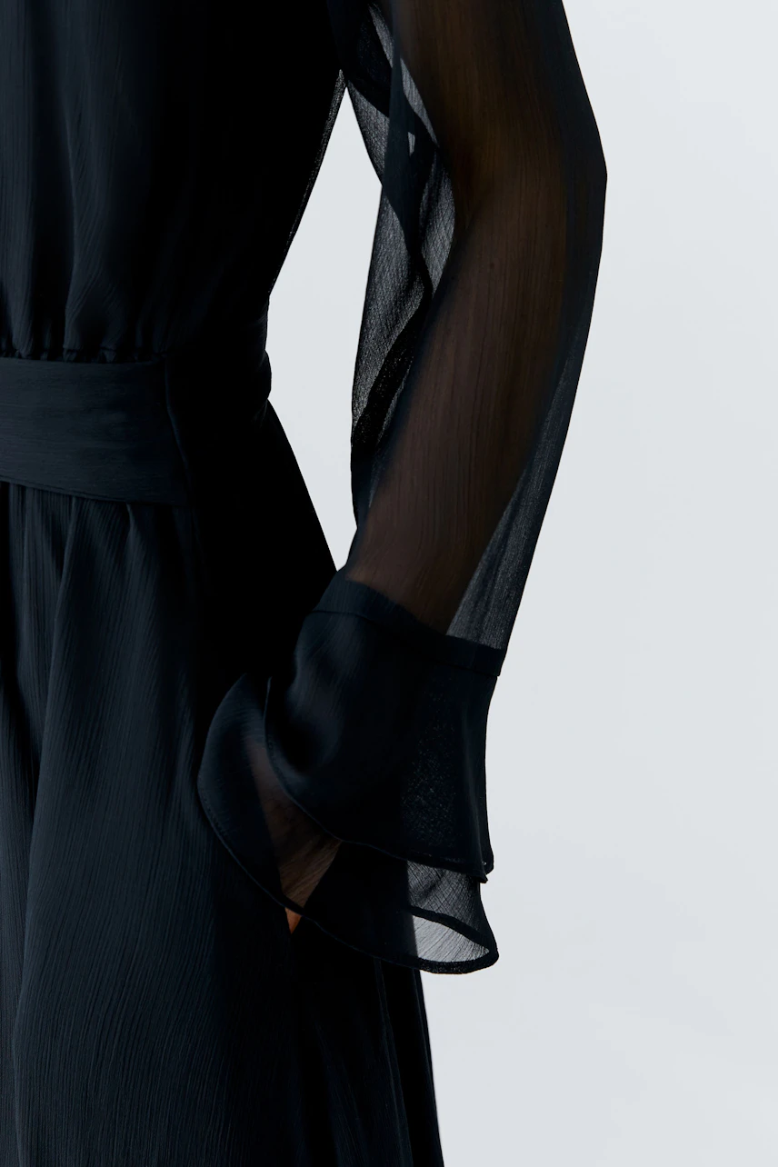 Maxikleid: Detailaufnahme eines schwarzen Maxikleid mit transparenten Ärmeln und lässigem Schnitt.