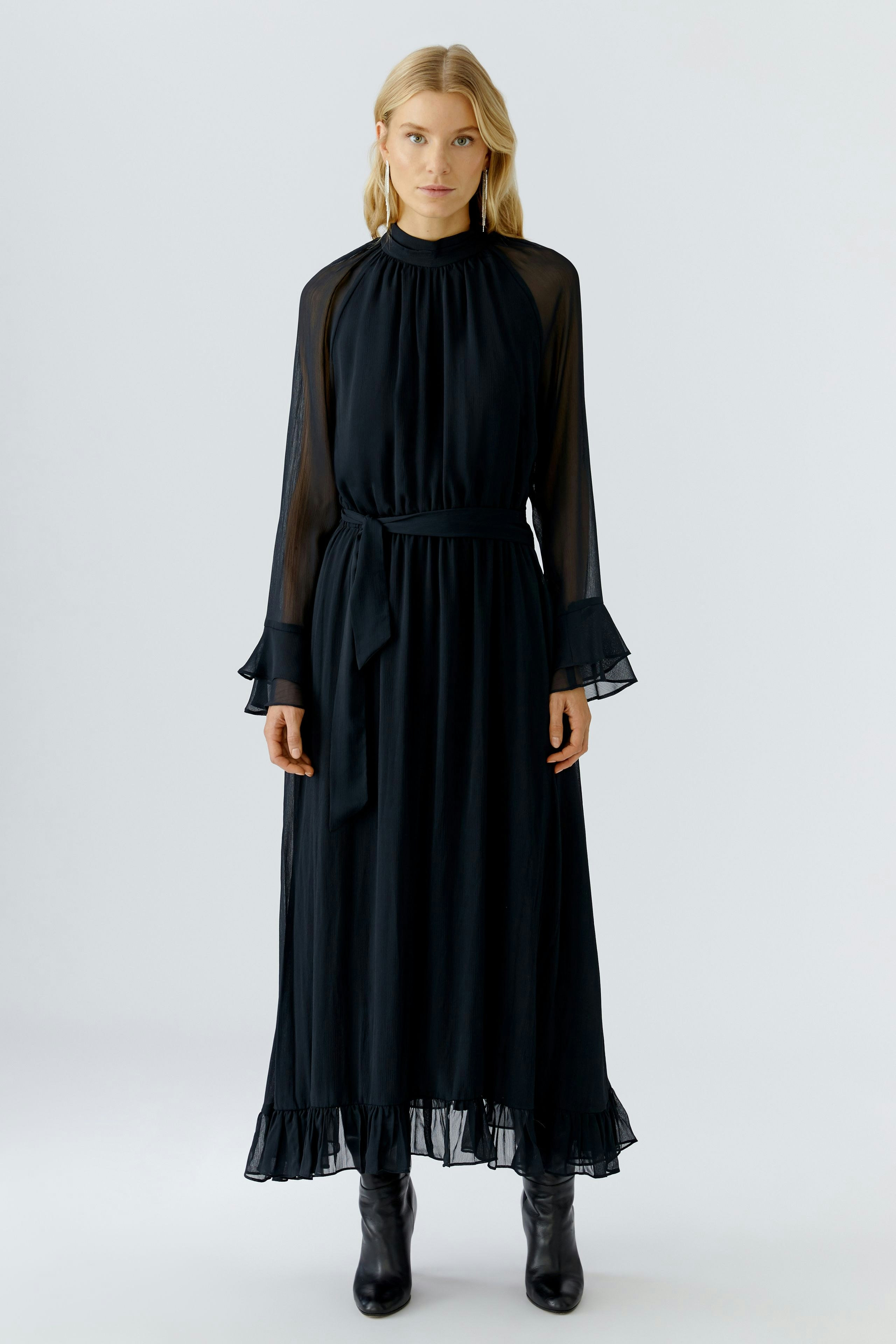 Maxi dress: Woman in a flowing black dress with sheer sleeves and a tied waist, standing confidently.
