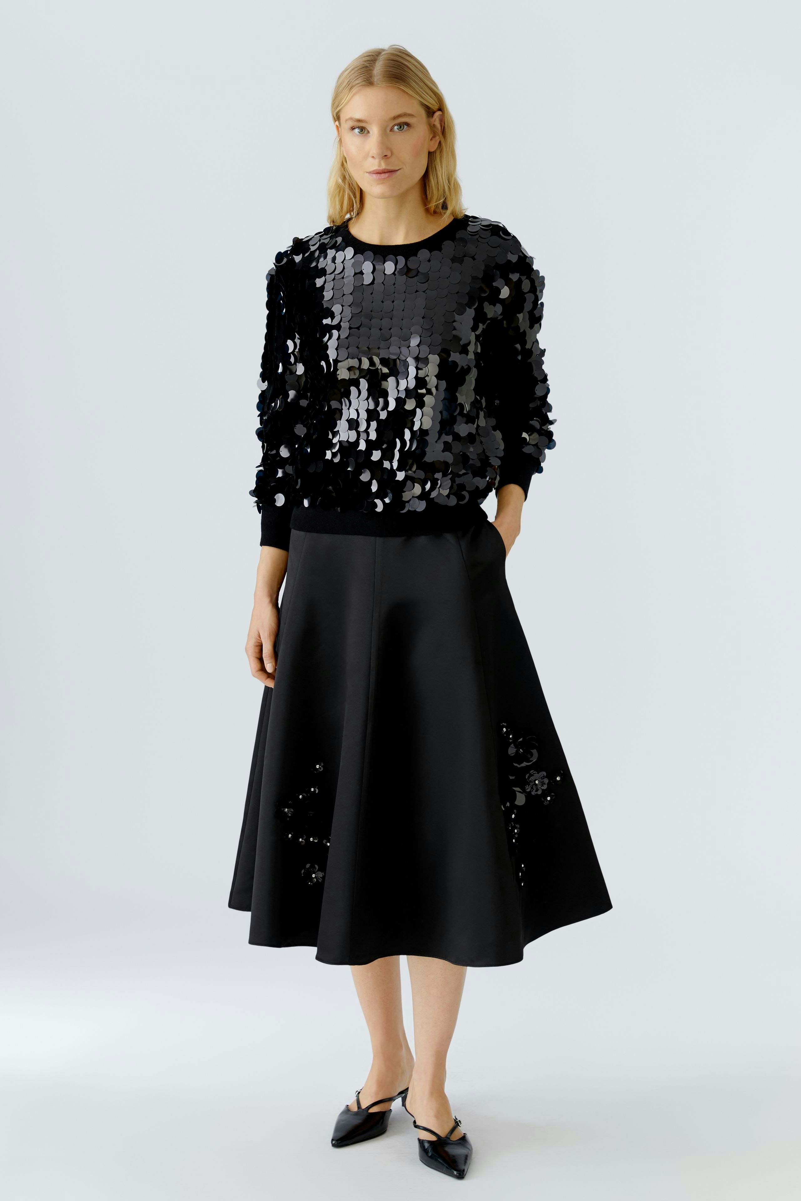 A-line skirt: Woman in a black sequined pullover and a flowing black A-line skirt.