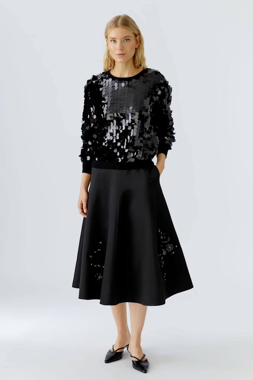 A-line skirt: Woman in a black sequined pullover and a flowing black A-line skirt.