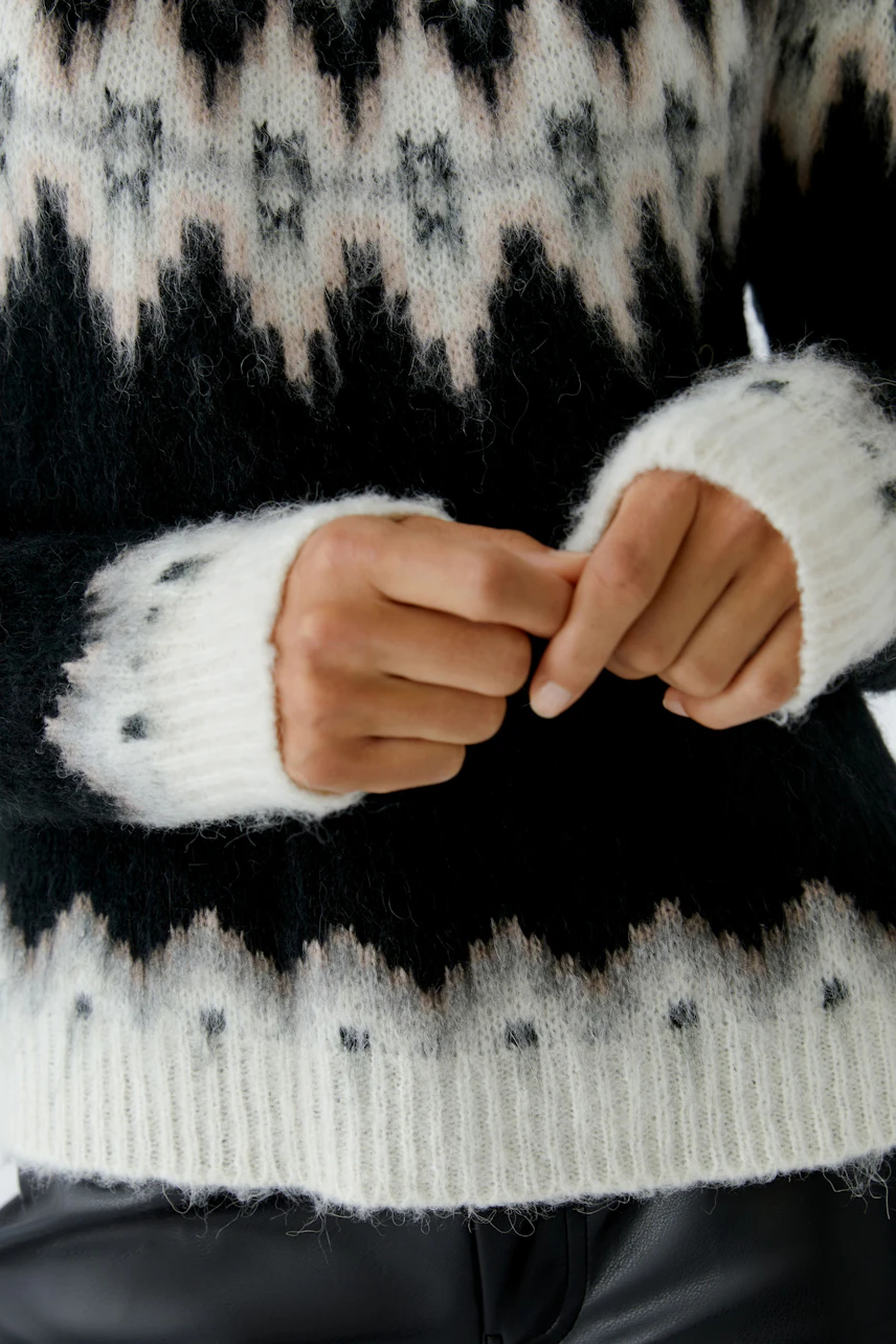 Damen-Pullover: Frau in einem schwarz-weißen Strickpullover mit geometrischem Muster und lässigem Schnitt.