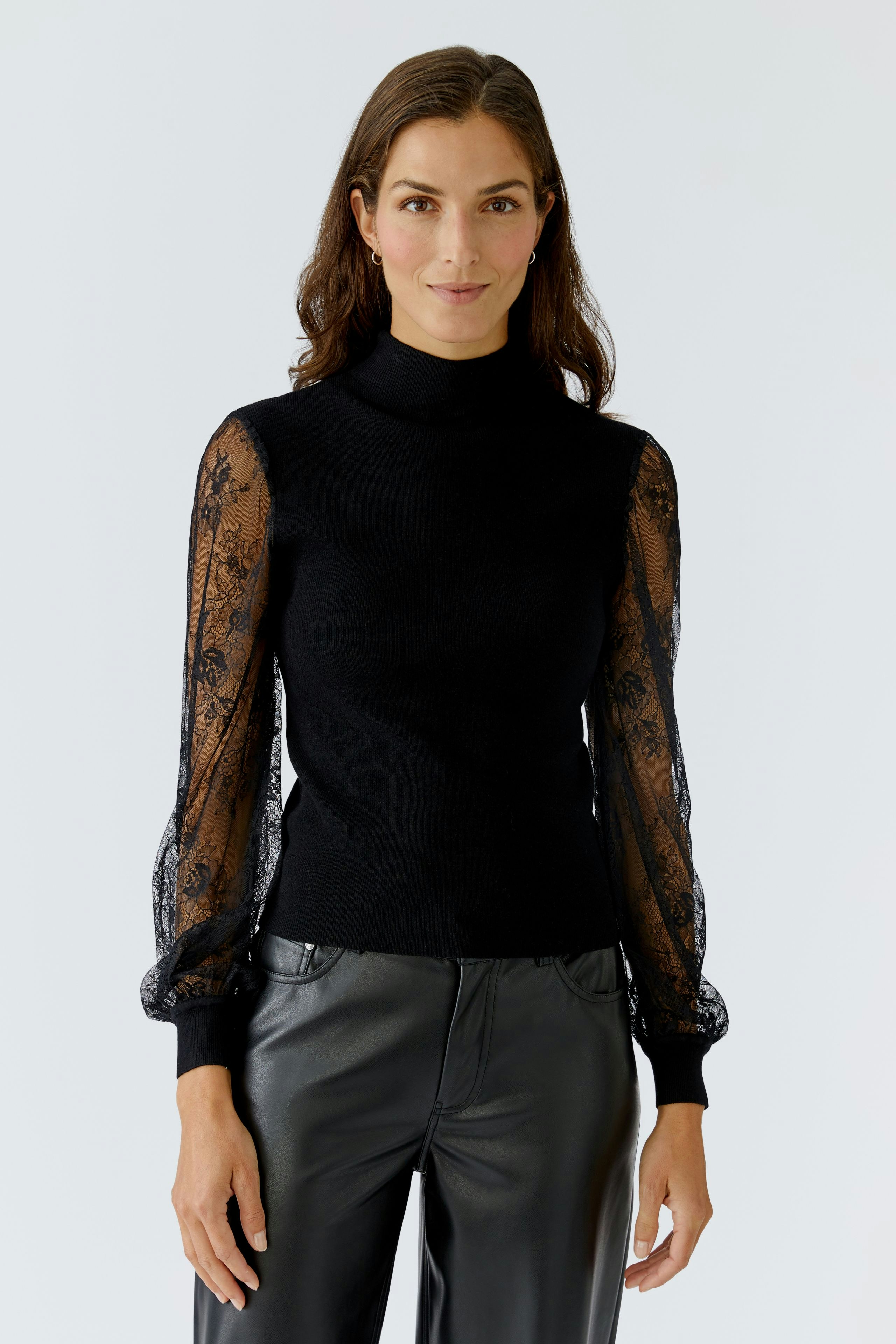 Modern women's pullover: Woman in black pullover with lace sleeves, paired with sleek leather pants.