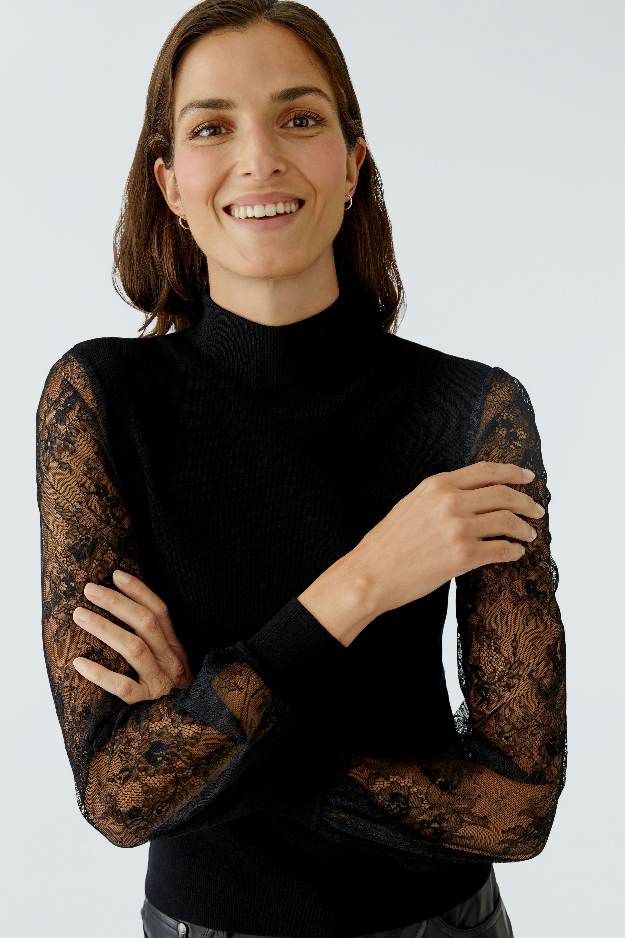 Modern women's pullover: A woman smiles in a black pullover with lace sleeves, showcasing a stylish look.