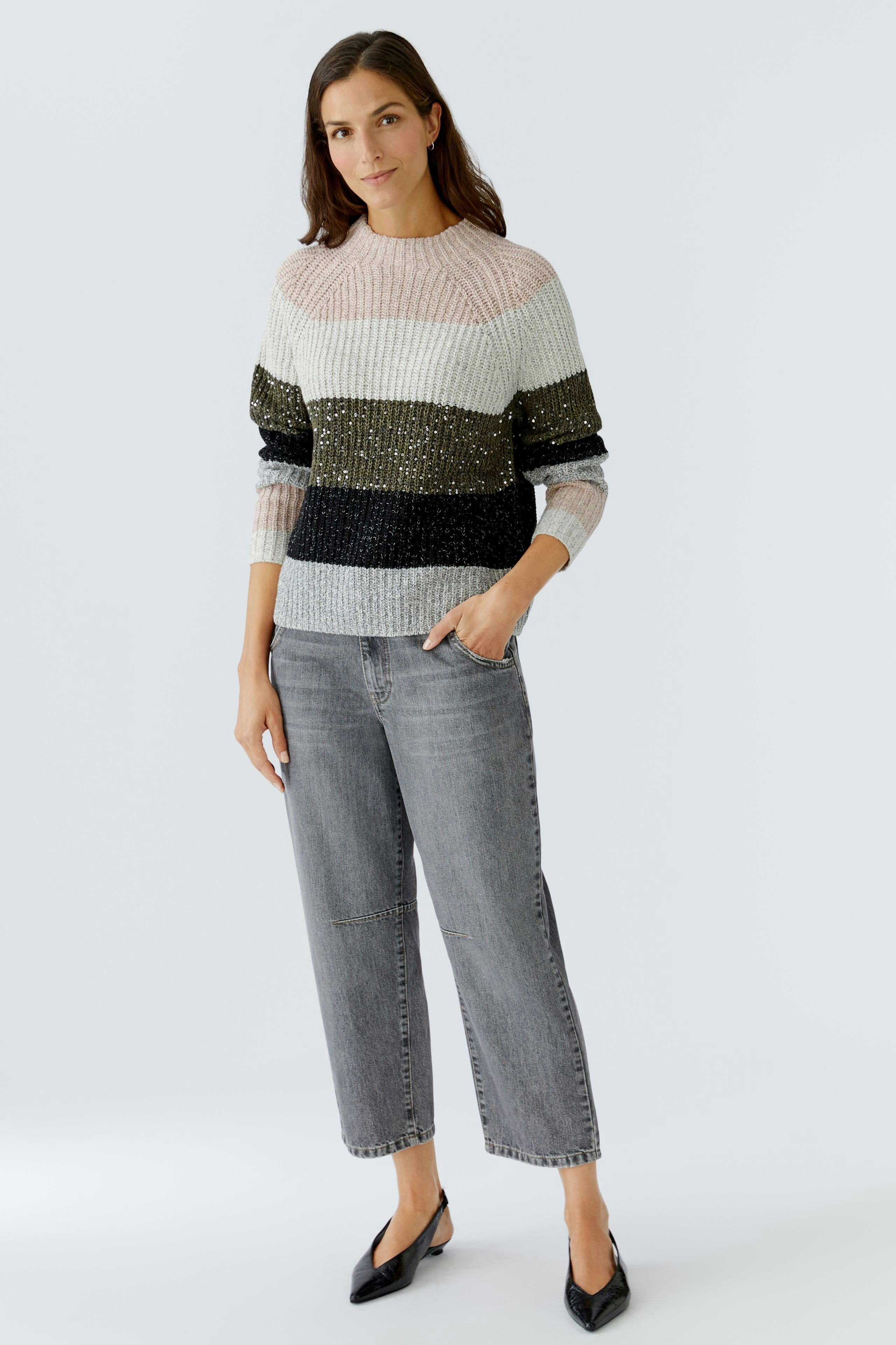Casual women's pullover: Woman in a striped pullover with sparkles, paired with gray jeans.