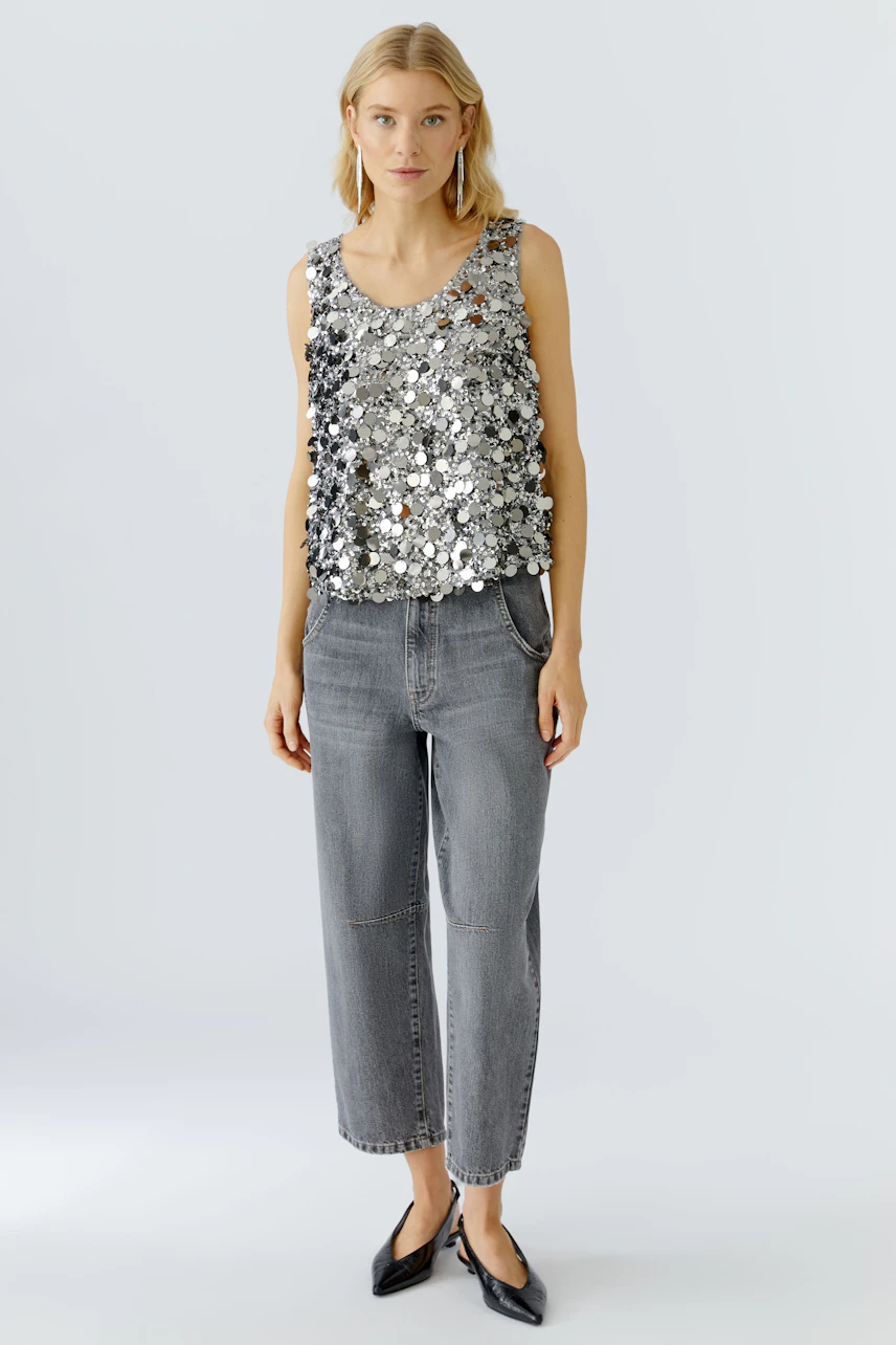 Feminines Top: Frau trägt ein glitzerndes Top mit Pailletten und lässigen Jeans.