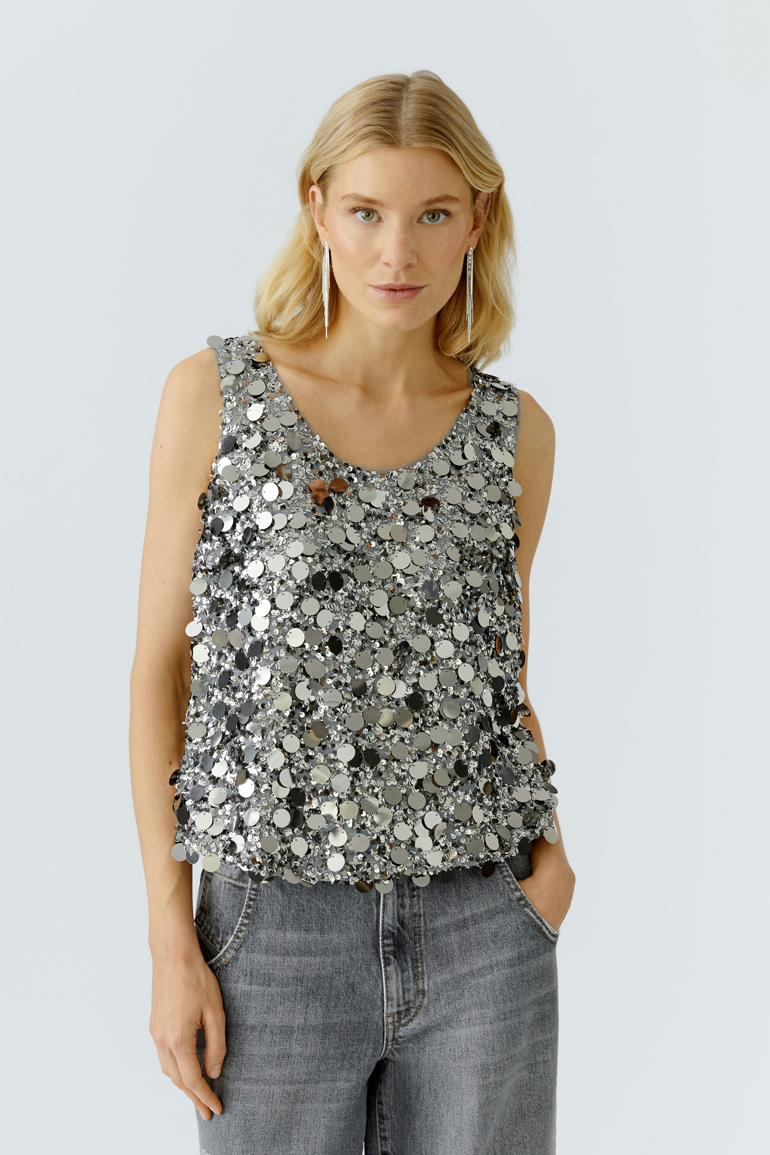 Trendy women's top: Young woman in a silver sequin tank top paired with casual jeans.