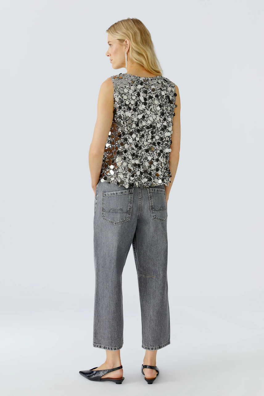 Damen-Top: Frau trägt ein glitzerndes Top mit floralen Details und lässigen Jeans.