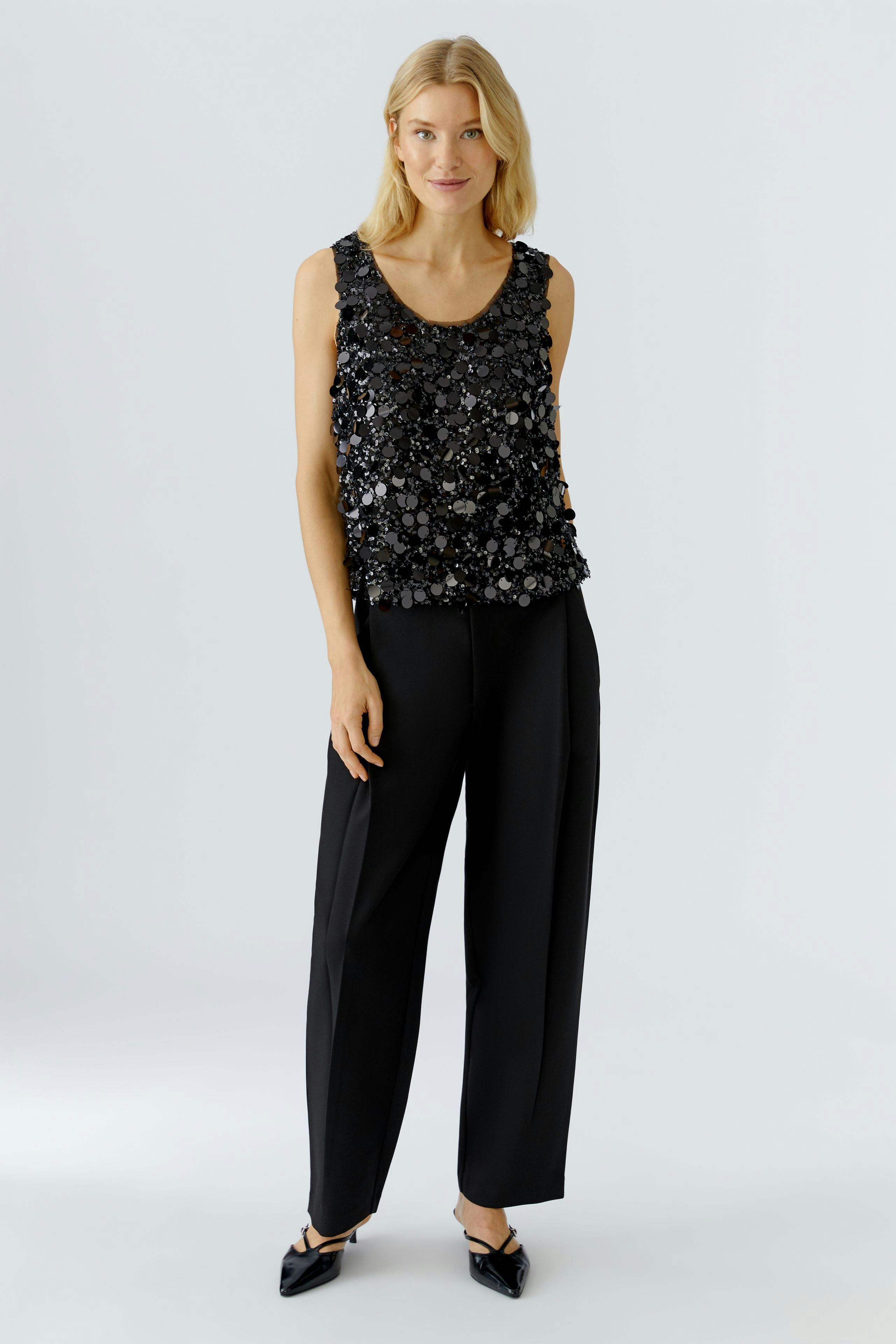 Stylish women's top: A woman in a black sequined tank top paired with loose black trousers.