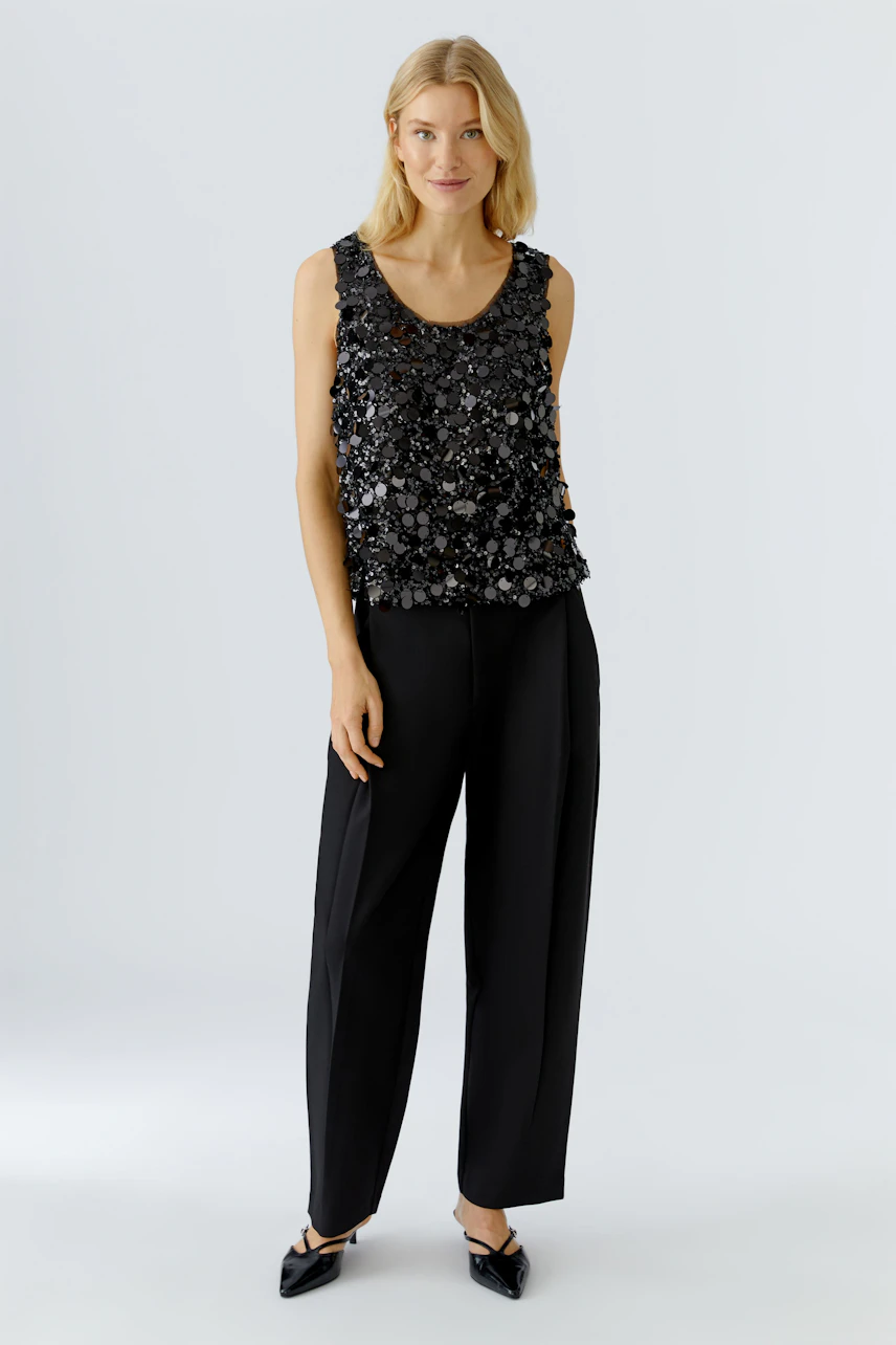 Schwarzes Damen-Top mit funkelnden Details, lässig kombiniert mit weiten Hosen.